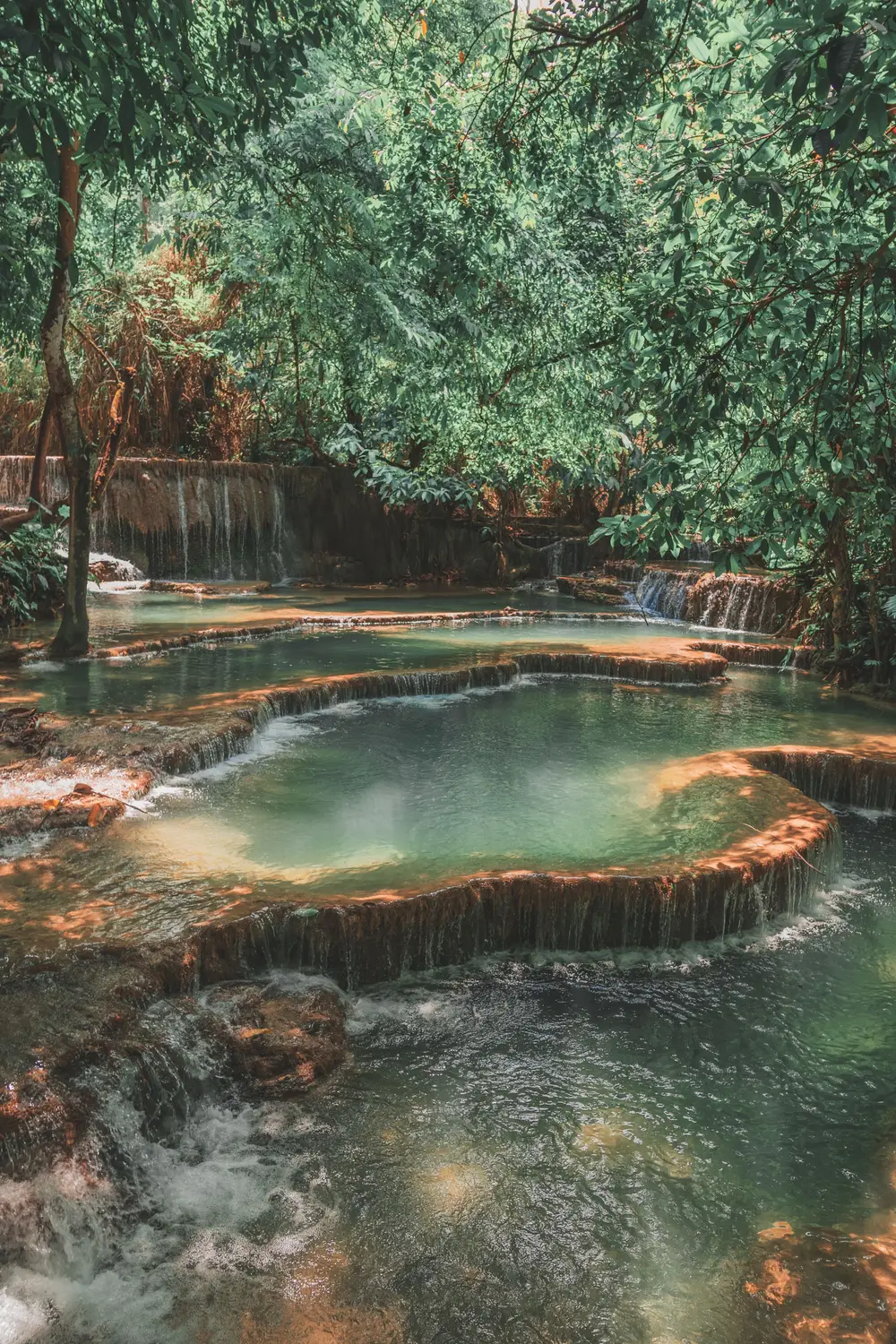 Turquoise pools of the Kuang Si waterfall surrounded by lush green forest near Luang Prabang, Laos.