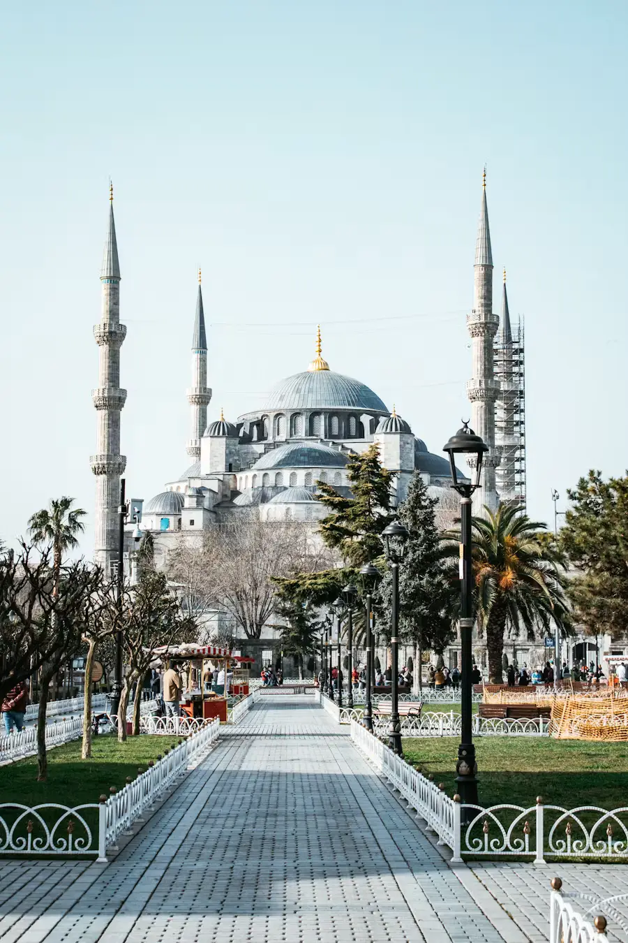 A long paved walkway leading toward the Blue Mosque, with its domes and minarets visible in the distance under a clear sky.