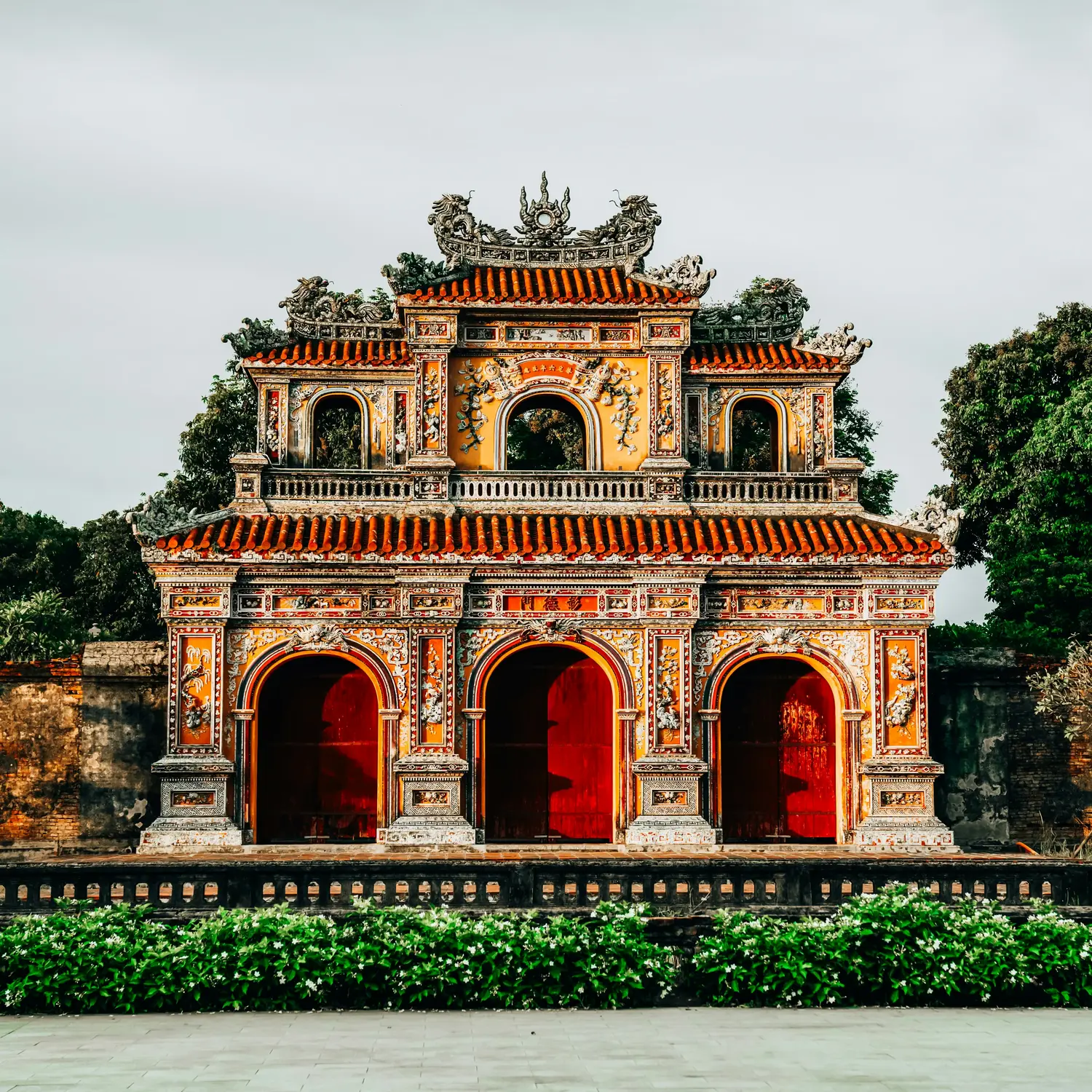 Ornate imperial gate of Hue Citadel with vibrant orange and red facades, intricate dragon carvings, and traditional Vietnamese tiered roof architecture, Vietnam