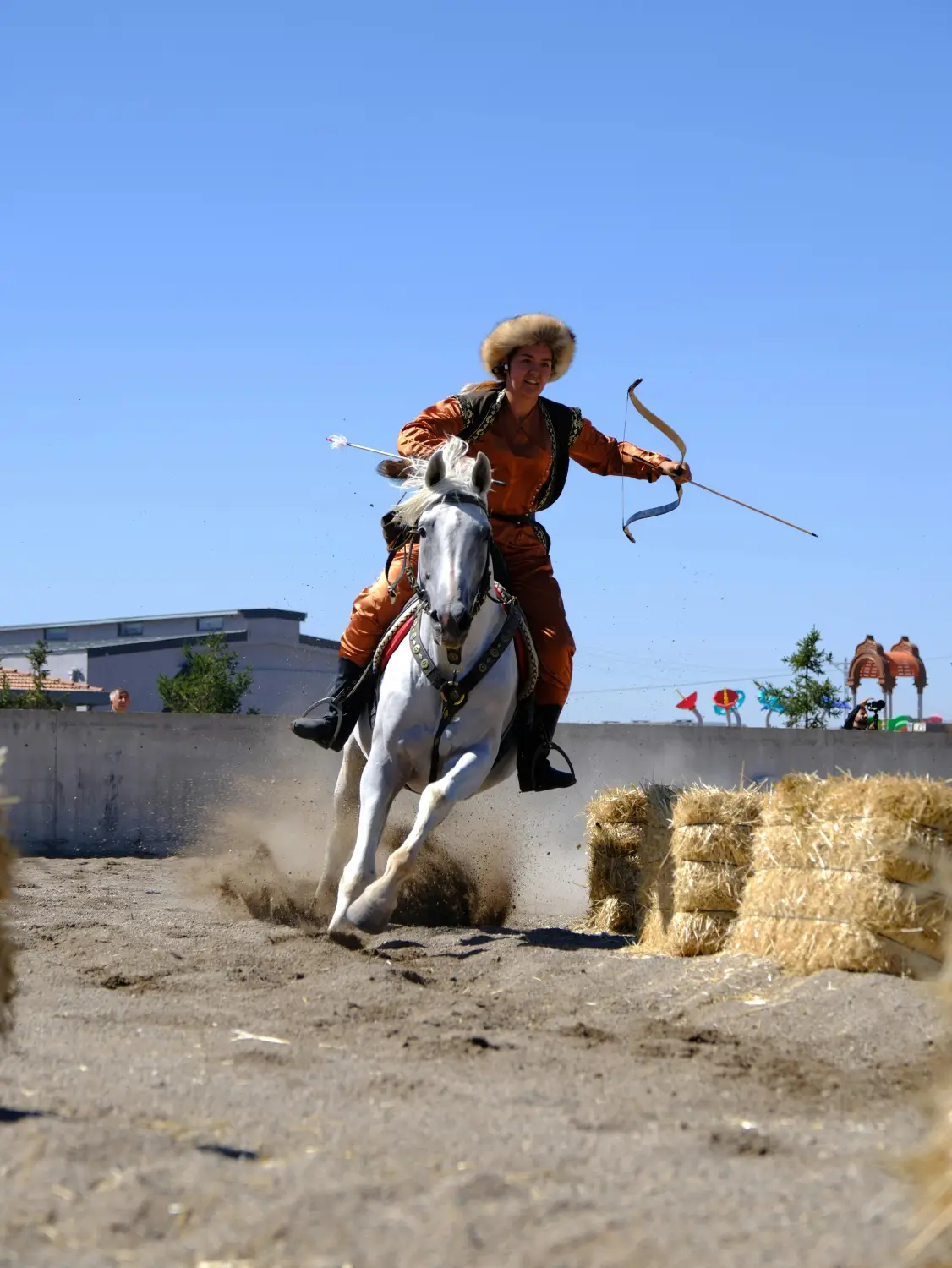 Mongolian woman in traditional orange deel costume performing horseback archery at full gallop during Naadam Festival, Mongolia