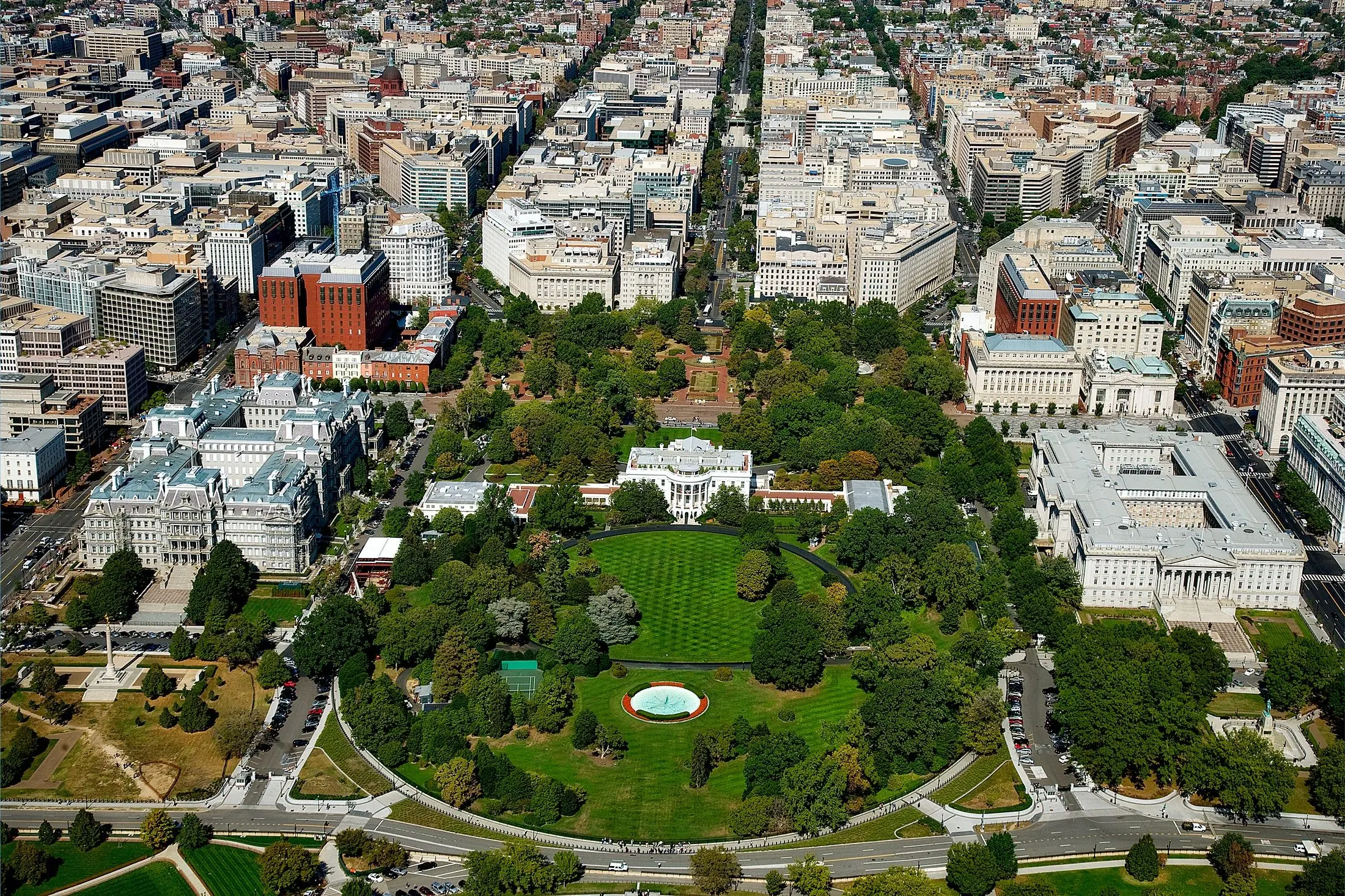 Aerial view of the White House and its grounds, surrounded by the tree-lined streets and buildings of Washington, DC.