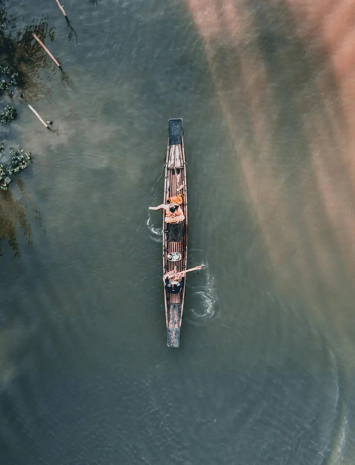 Aerial drone view of two people rowing a traditional wooden longboat on a river in Myanmar