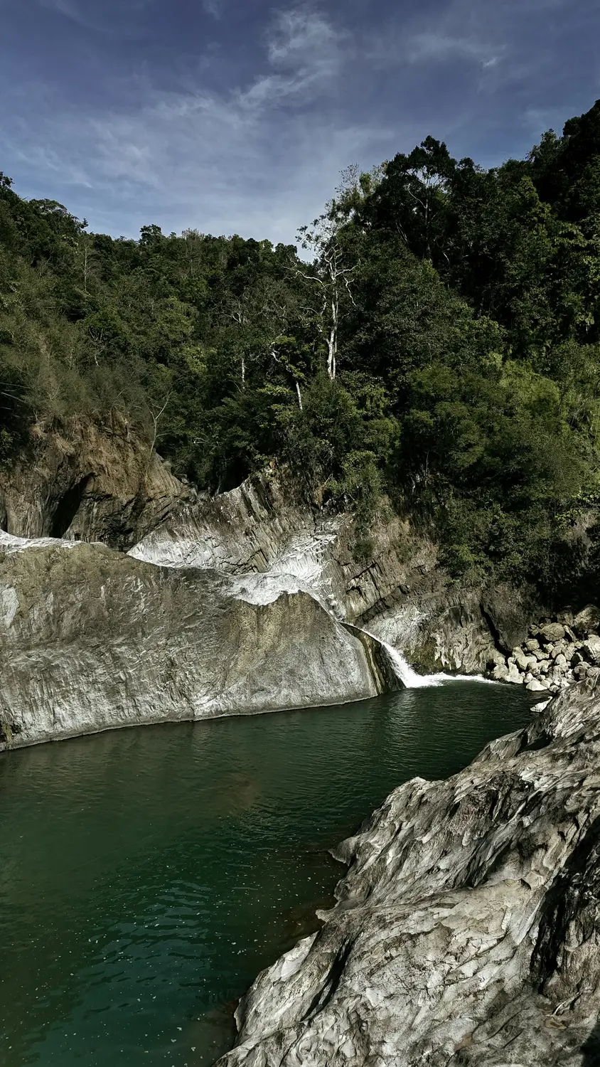 Emerald green river pool surrounded by forested cliffs and rocks in the Philippines.