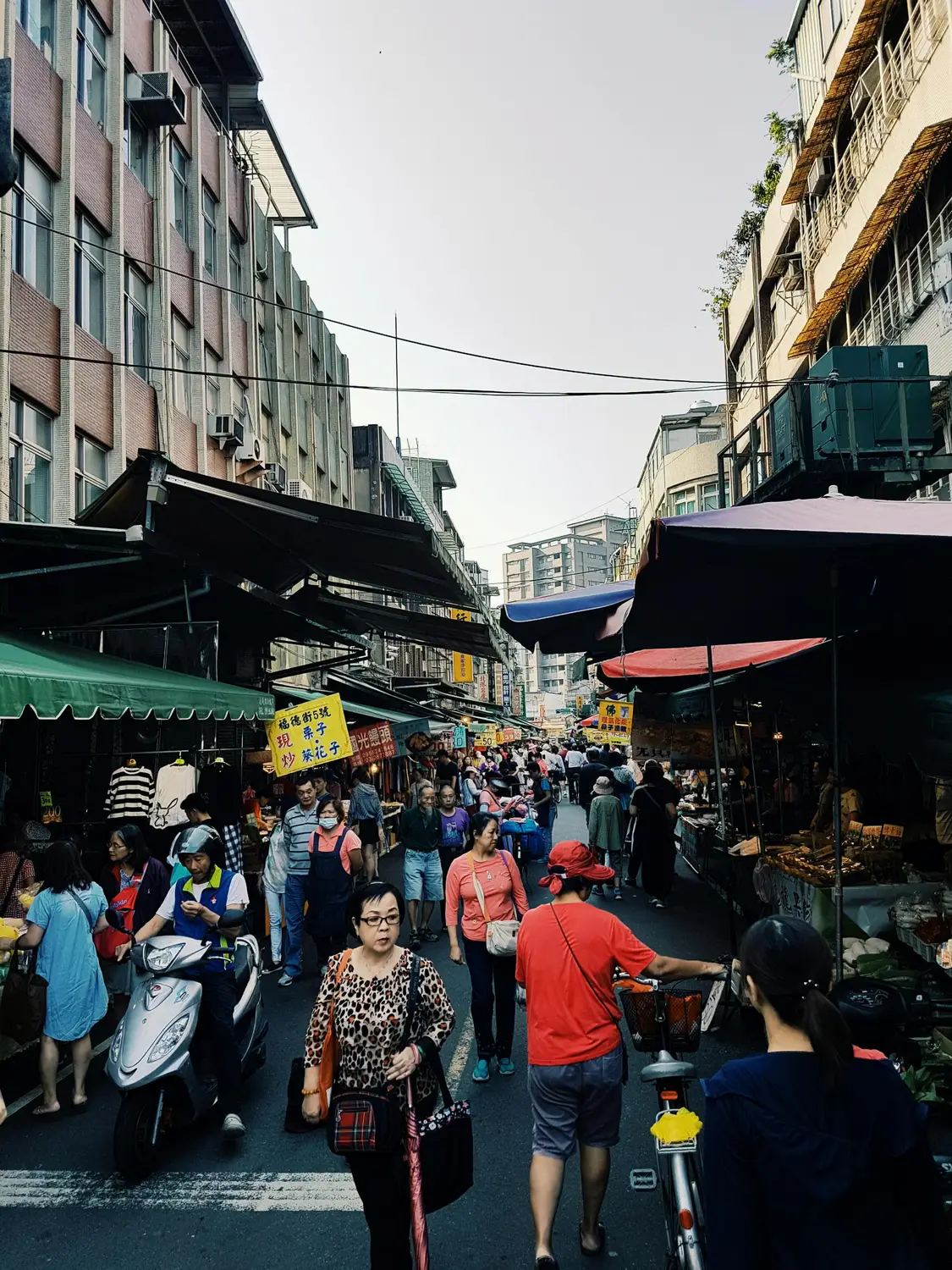 Crowded outdoor street market in Tainan, Taiwan, with shoppers walking past stalls under colorful awnings and Chinese signage