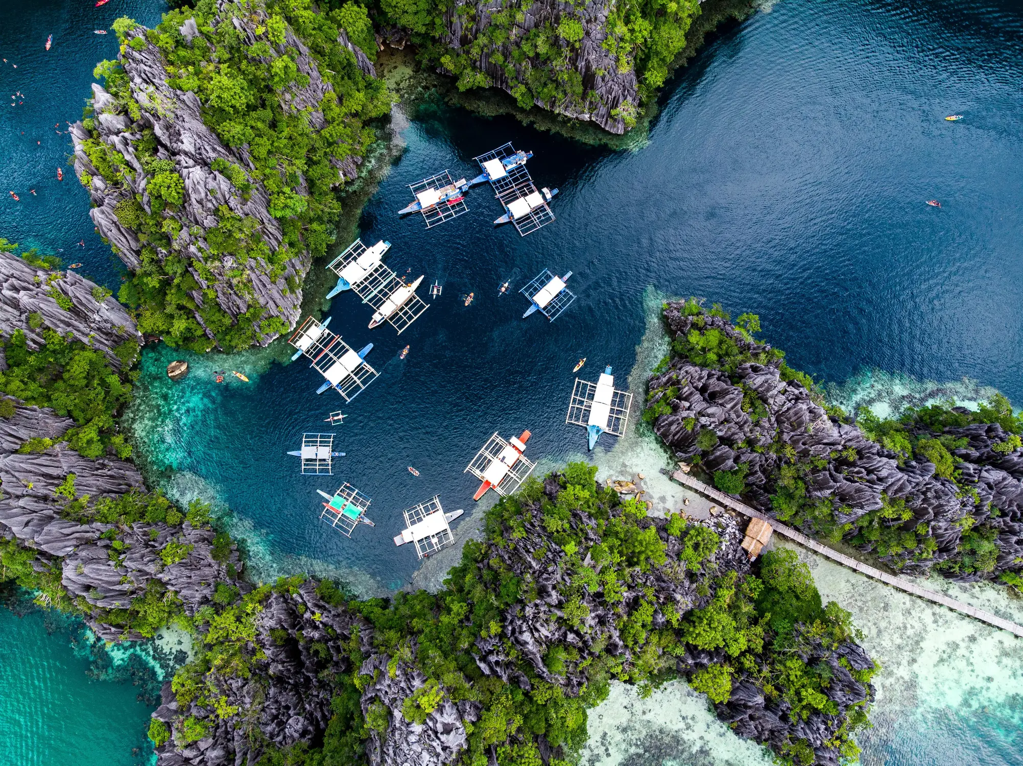 Aerial view of traditional outrigger boats anchored in a turquoise lagoon surrounded by rugged limestone karst cliffs and greenery in Coron, Palawan, Philippin…Aerial view of traditional outrigger boats anchored in a turquoise lagoon surrounded by rugged limestone karst cliffs and greenery in Coron, Palawan, Philippines.