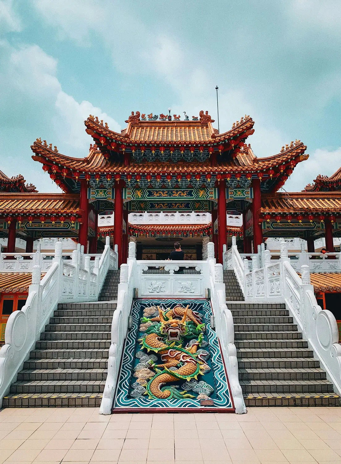 Traditional Chinese temple ornate red and gold entrance gate with decorative stairs and blue sky in Malaysia