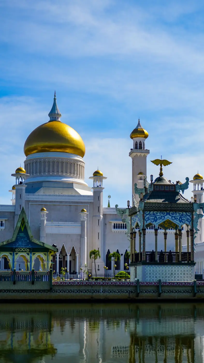 Omar Ali Saifuddien Mosque golden dome with ornate royal barge pavilion viewed from lagoon, Bandar Seri Begawan Brunei