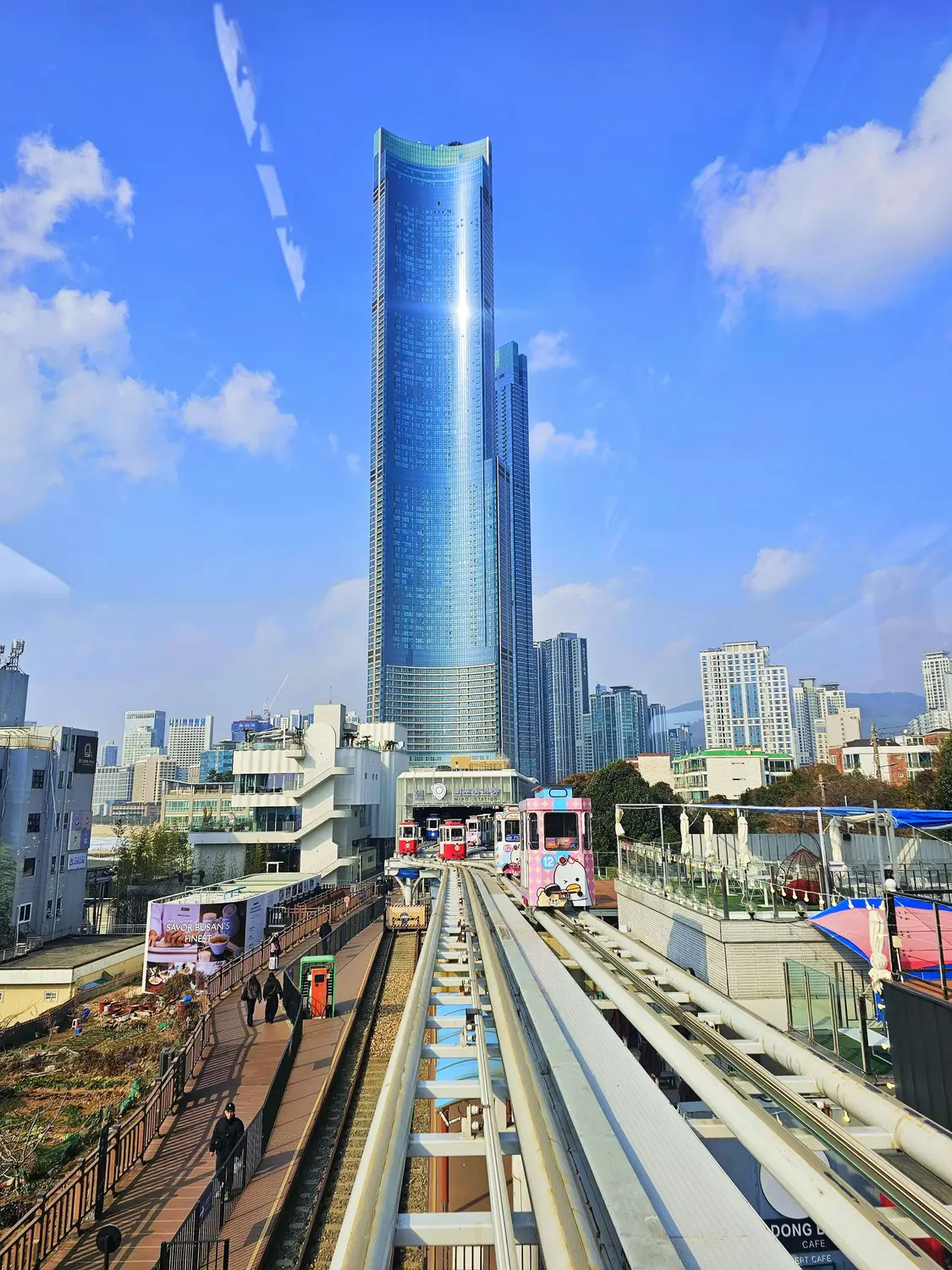 Modern skyscraper towering over an elevated railway and city buildings under a blue sky in South Korea.