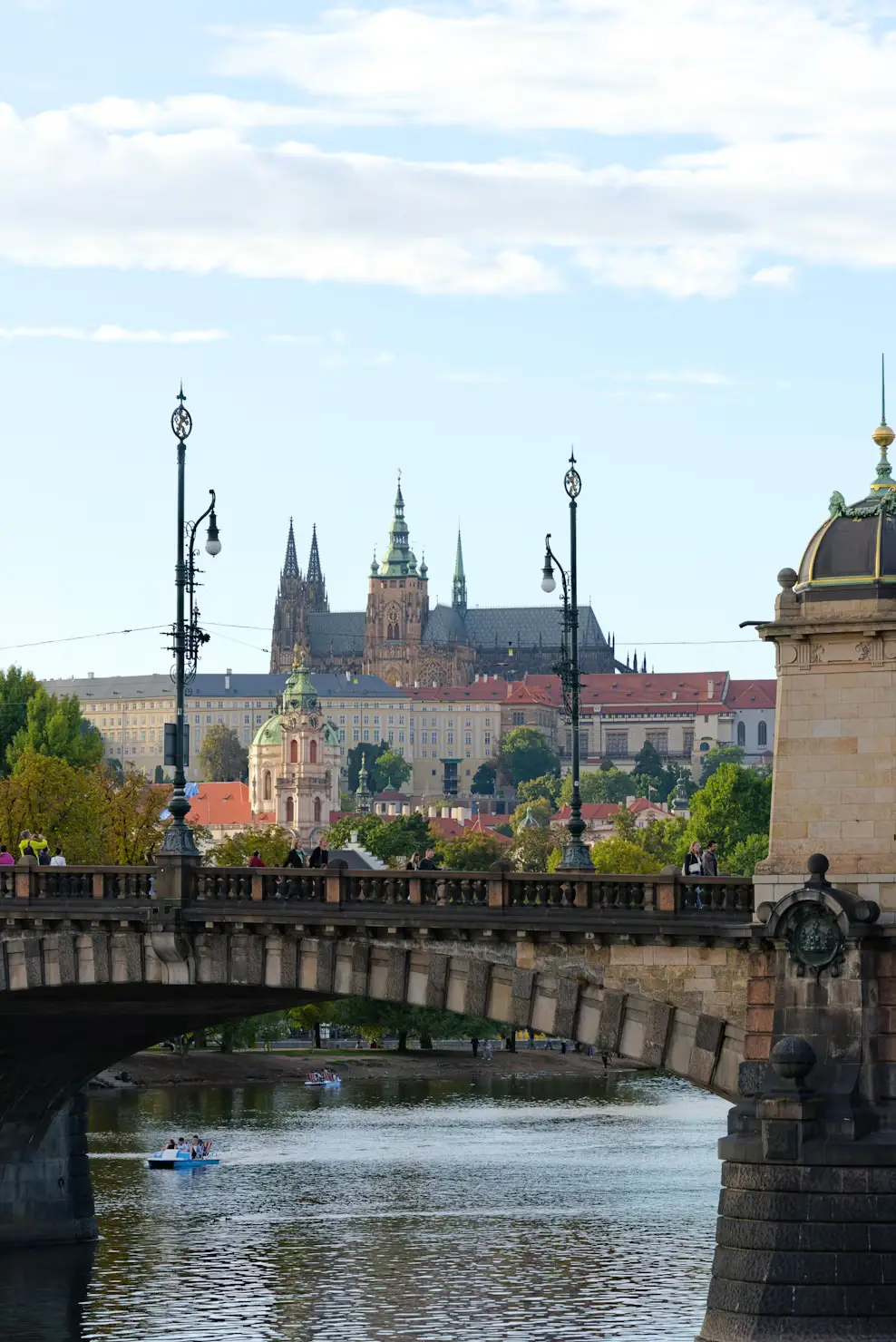 View through a stone bridge arch of Prague Castle and colorful riverside buildings along the Vltava