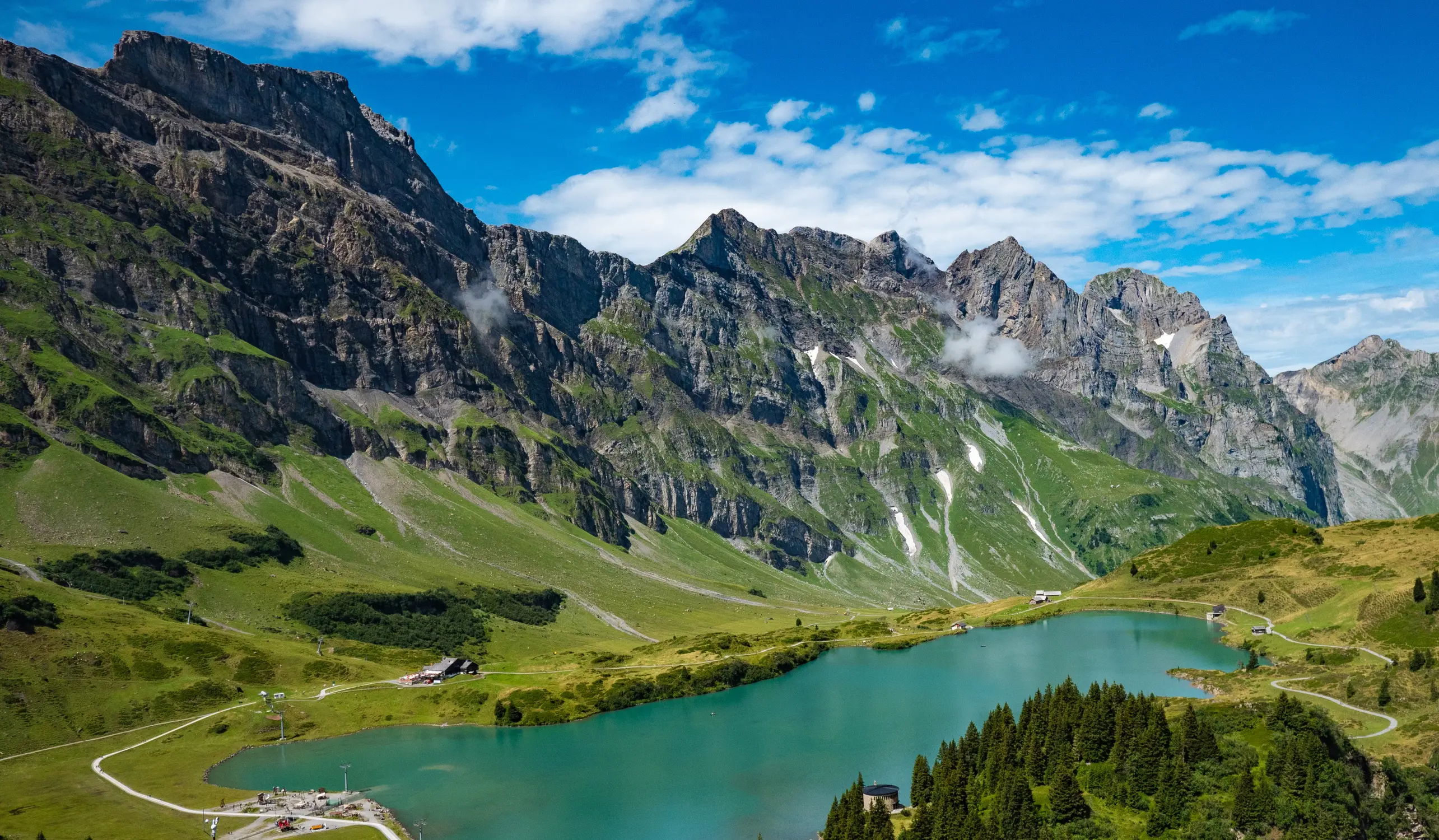 Turquoise alpine lake surrounded by green meadows and rugged mountain peaks, Swiss Alps