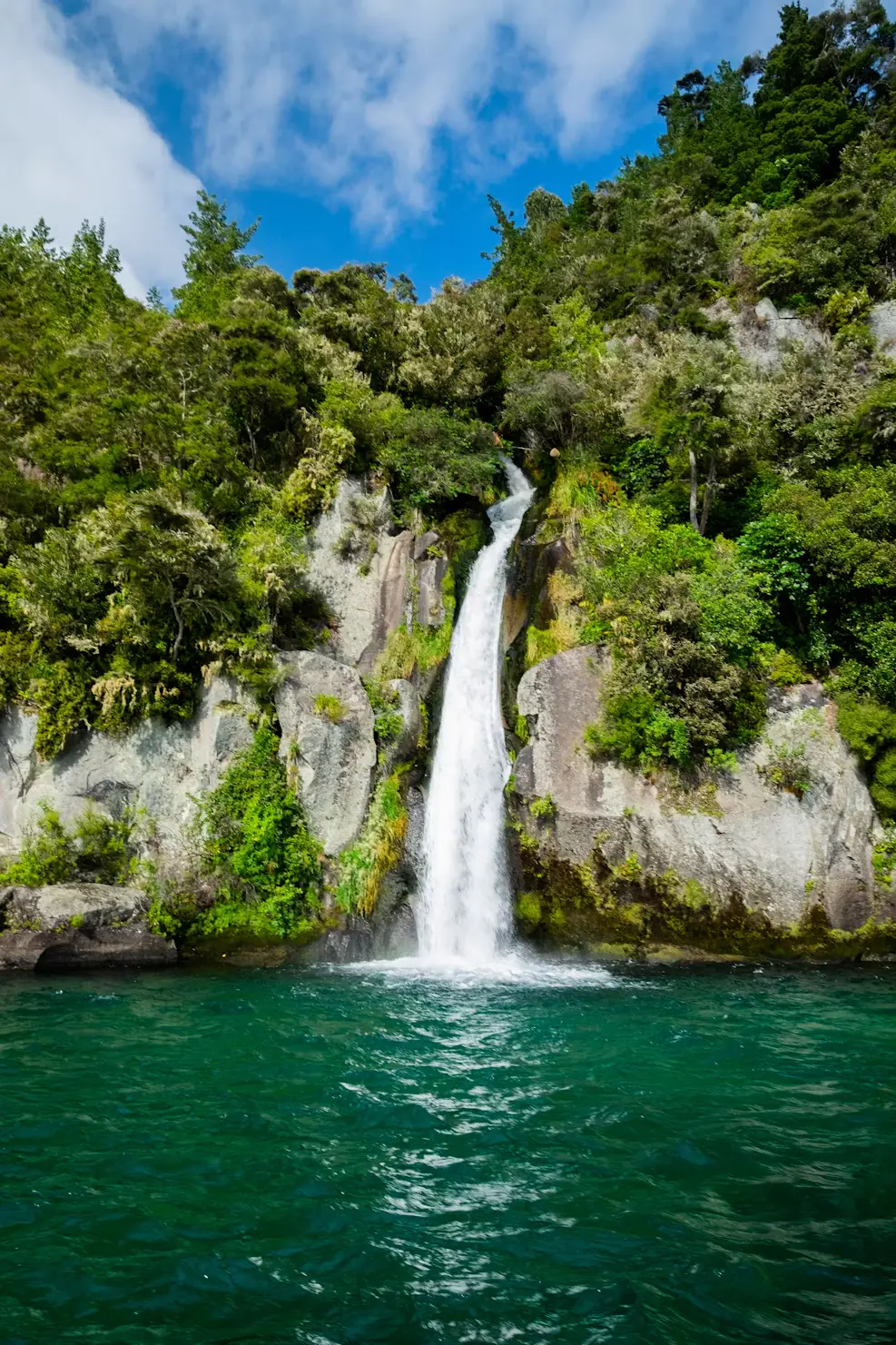 Tall waterfall cascading into a clear turquoise pool surrounded by lush forest.
