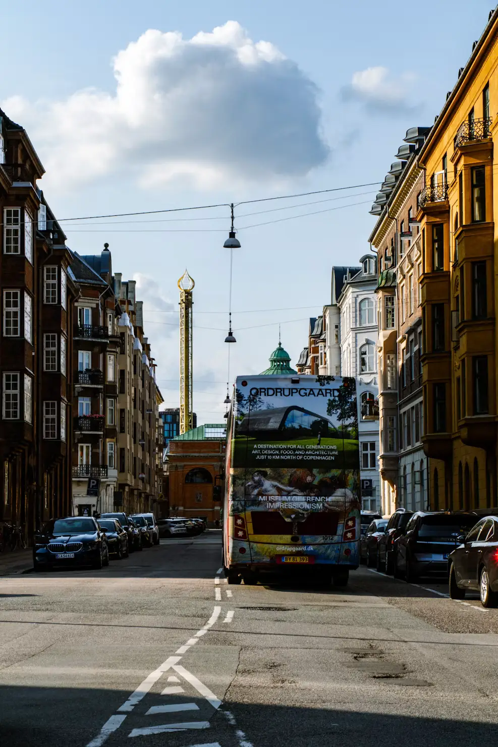 Street view of a colorful Danish town with a tour bus and a column monument