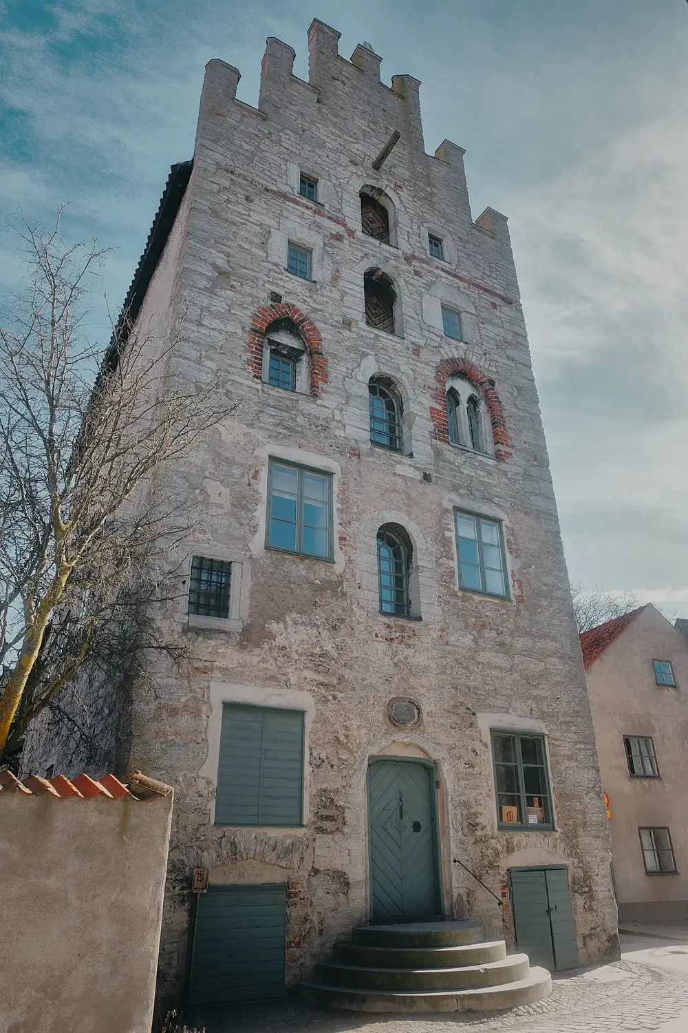 Tall narrow stone tower building with crenellated top and small arched windows, against a cloudy sky.