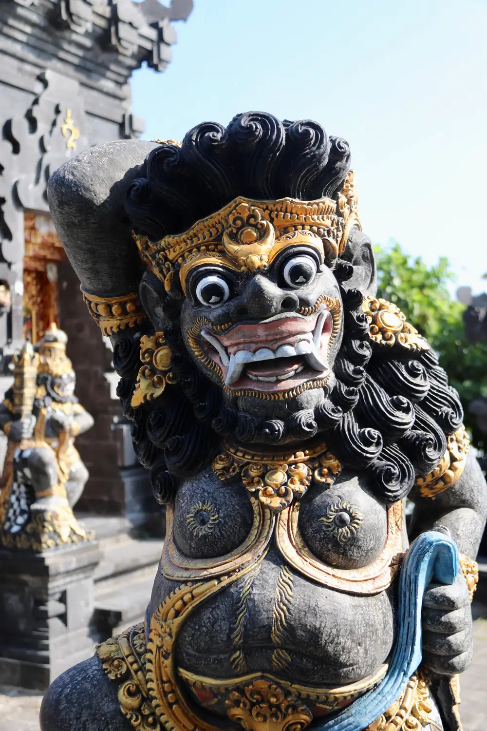 Traditional Balinese guardian statue with ornate gold detailing and a fierce carved face, standing at a temple entrance in Bali, Indonesia.