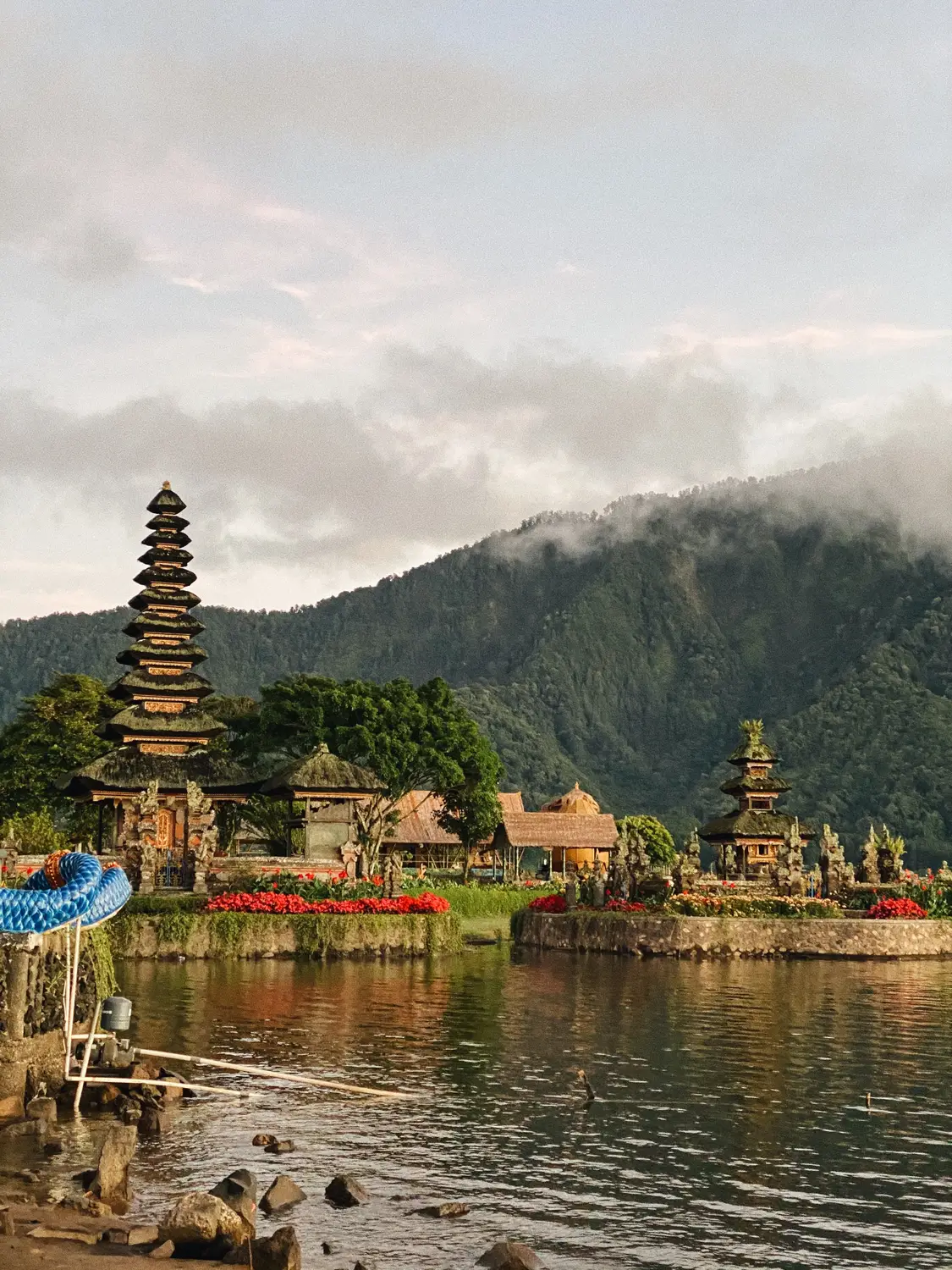 Lakeside Balinese temple complex with tiered meru shrines set against misty mountains and calm water in Bali, Indonesia.