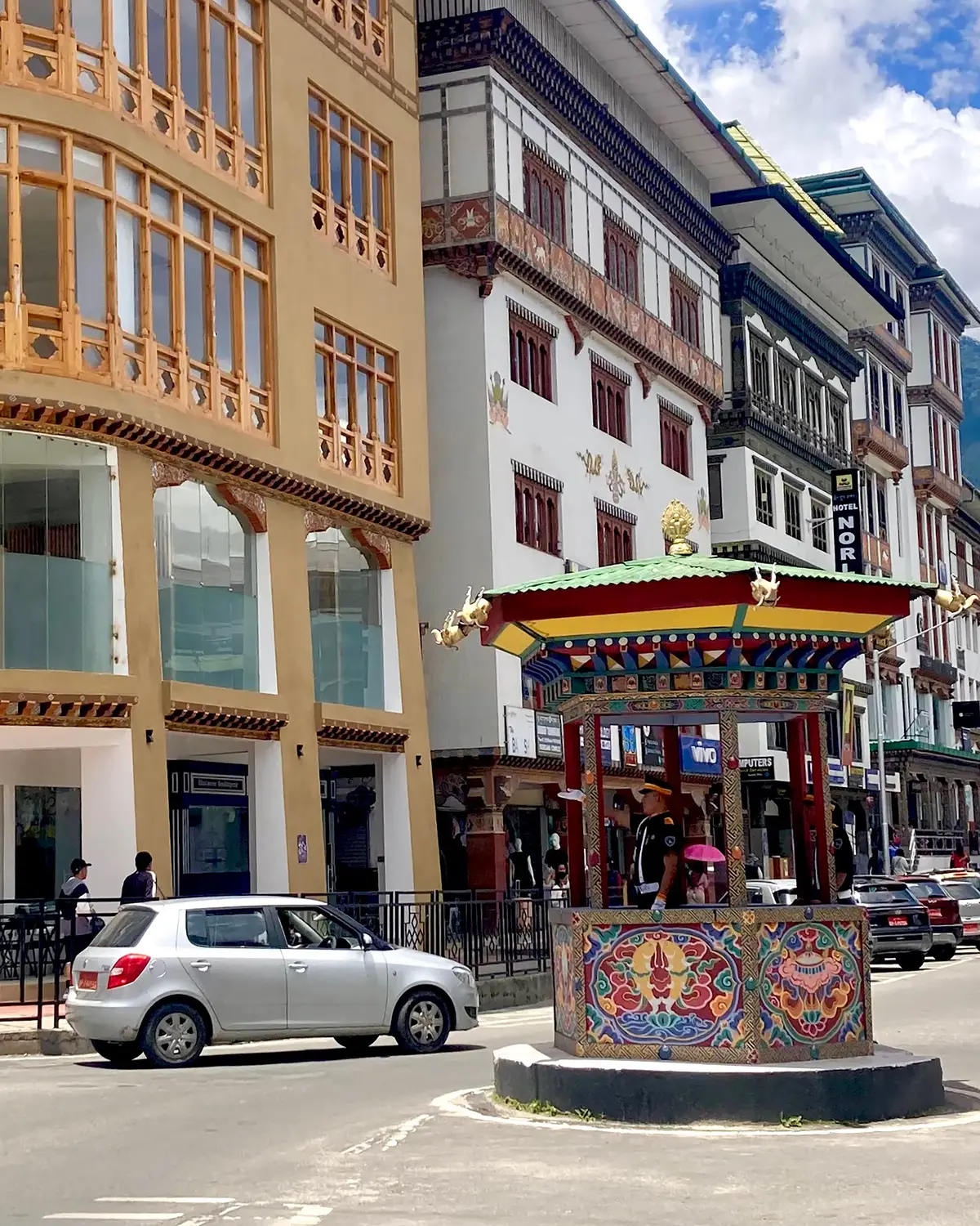 Traditional Bhutanese town street with decorated buildings, shops, and a painted roundabout in Bhutan.