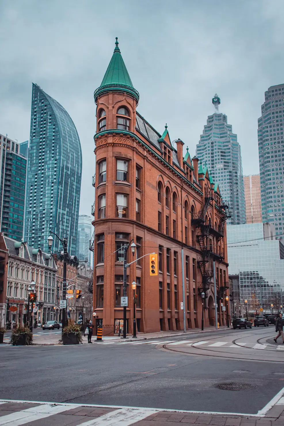 The historic red-brick Gooderham (Flatiron) Building at a city intersection, with modern skyscrapers behind it.