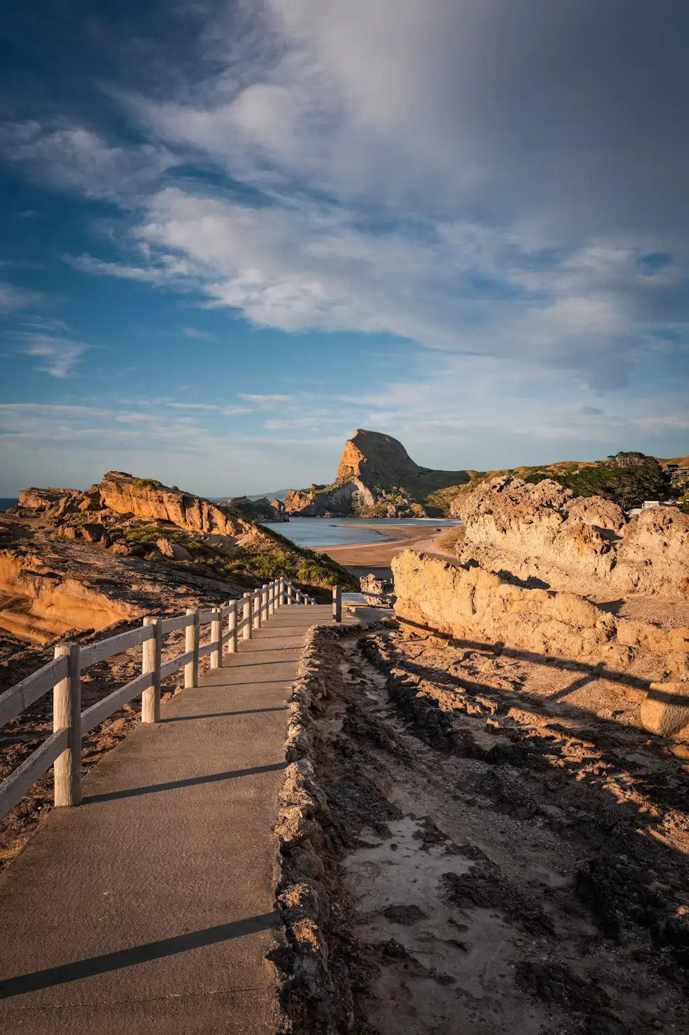 Boardwalk winding through rugged coastal rocks toward a sandy beach and sea stacks.