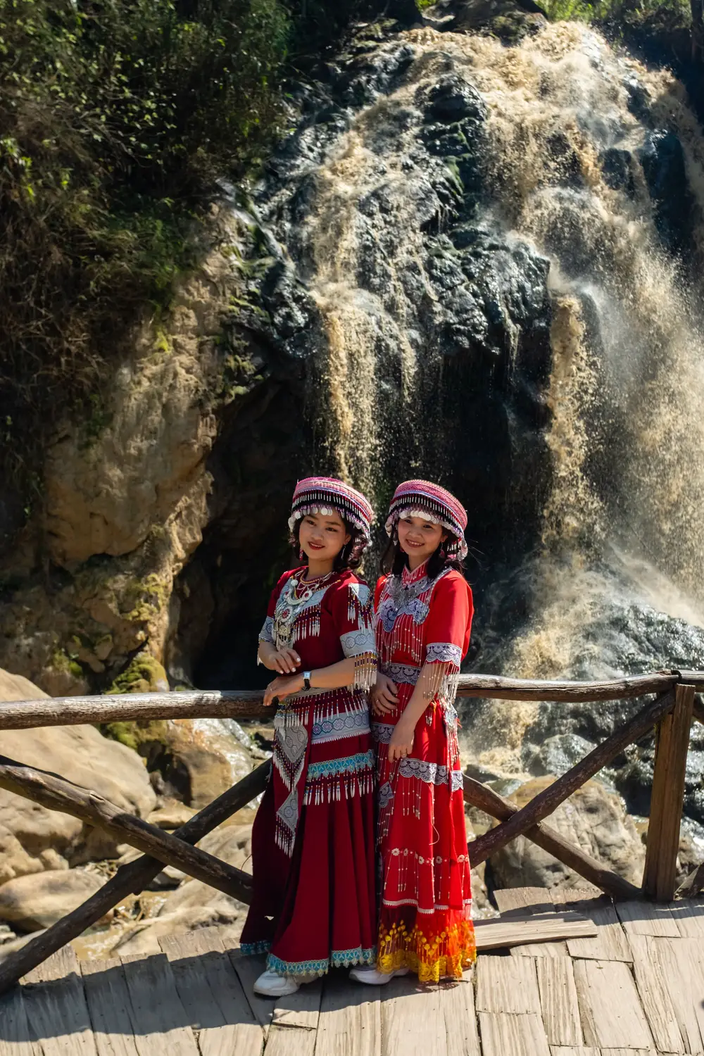Two women in traditional Lao dress posing in front of a waterfall in Laos.