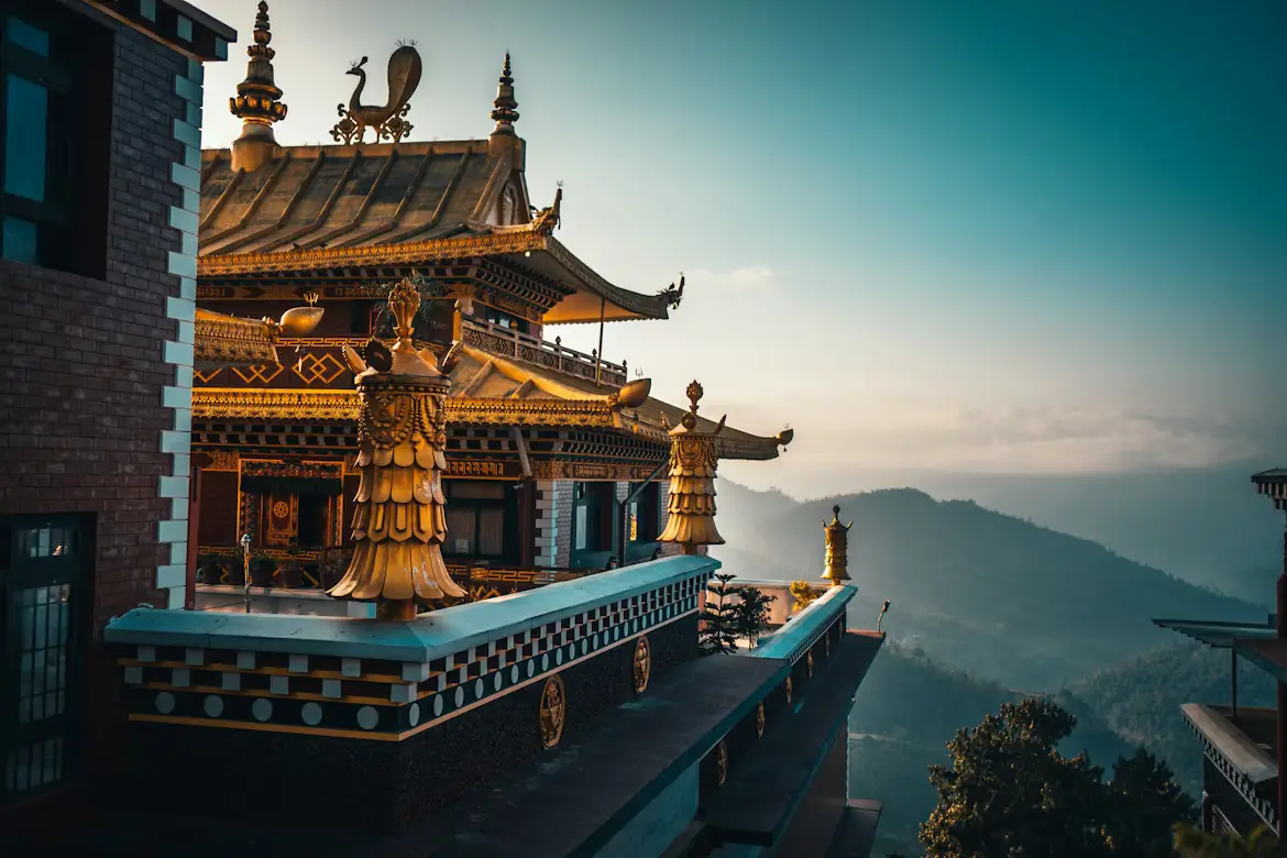 Ornate golden Buddhist monastery rooftop overlooking misty hills at sunset, Nepal