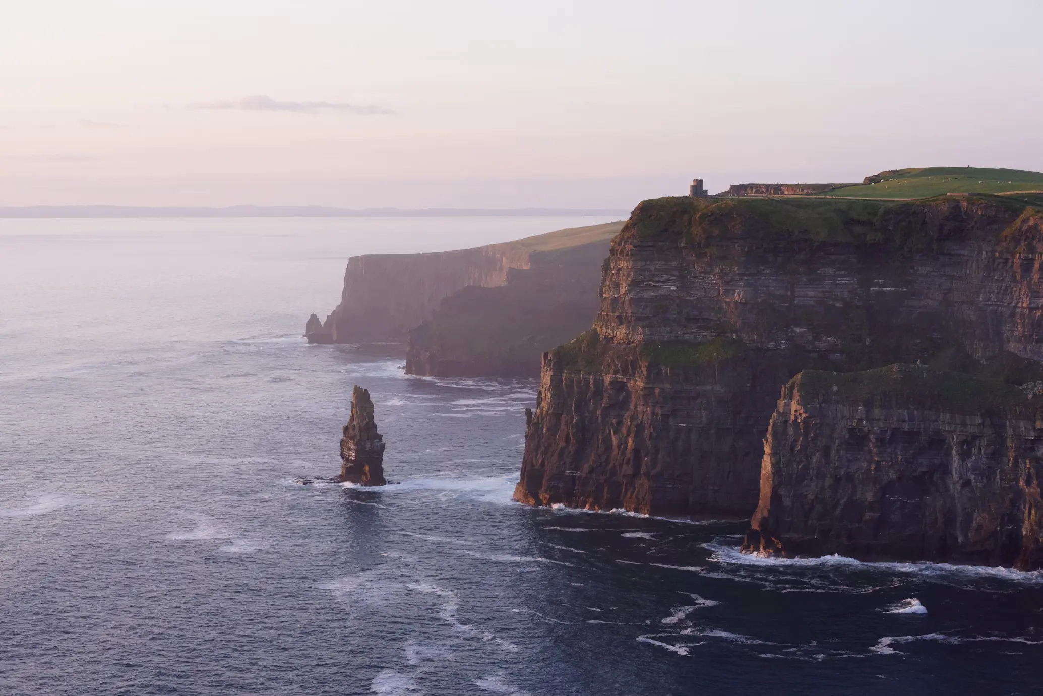 Rugged sea cliffs with a rock sea stack rising from the water, viewed in soft evening light, Cliffs of Moher, Ireland.