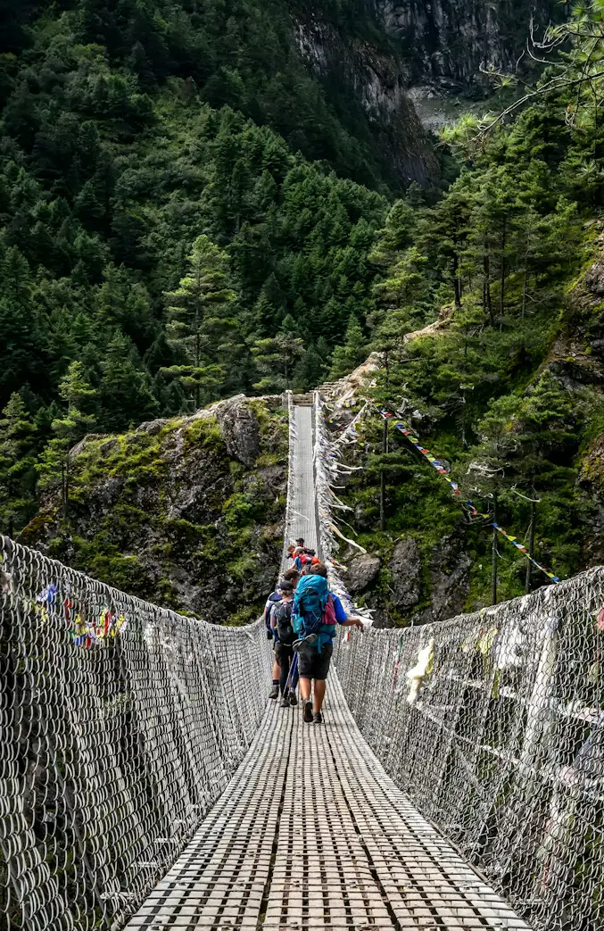 Trekker with backpack crossing a long suspension bridge over a forested gorge, Nepal Himalayas