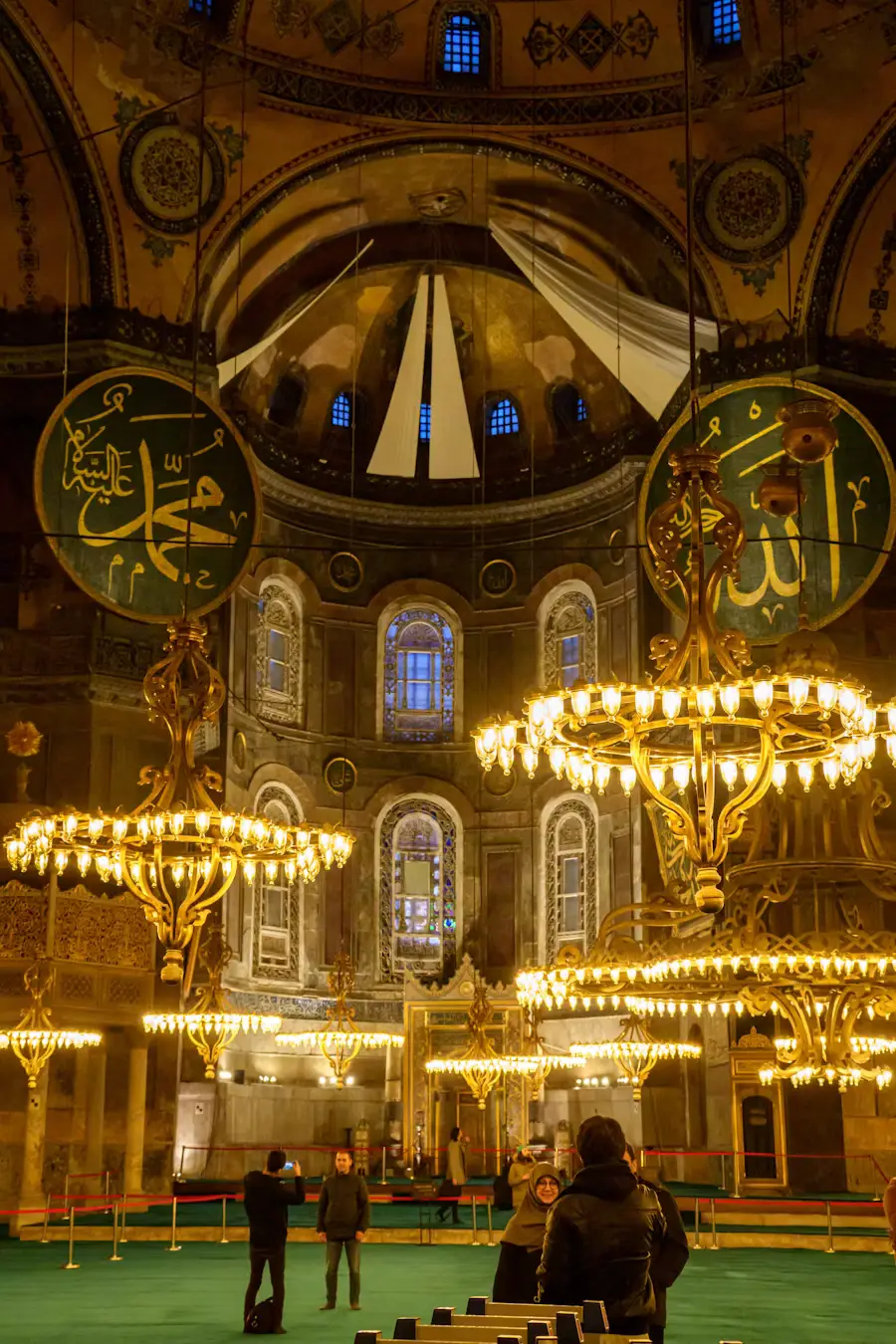 The ornate golden interior of Hagia Sophia, with intricate chandeliers and Arabic calligraphy medallions beneath the domed ceiling.