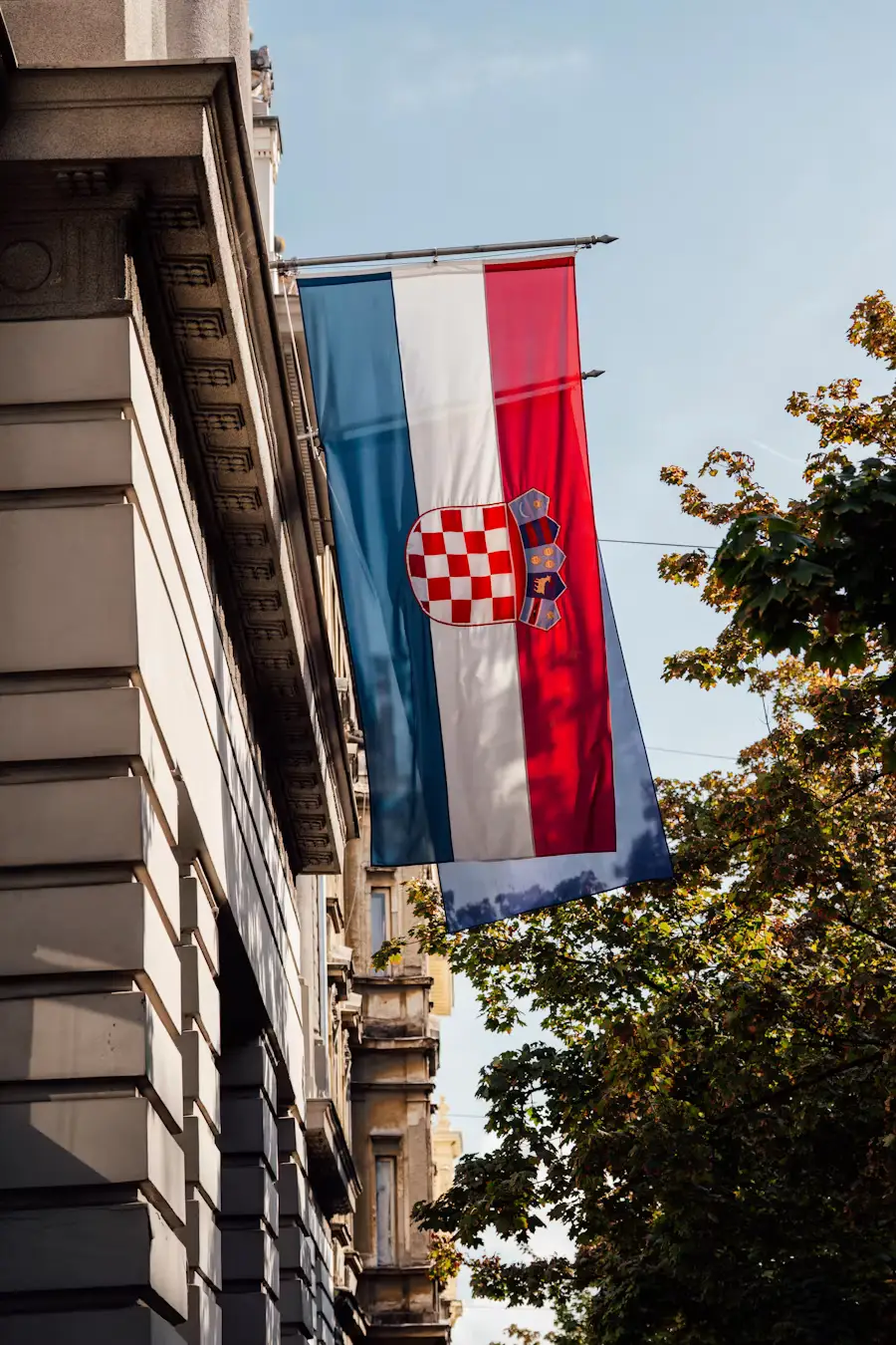 Croatian flag hanging from a stone building along a tree-lined street.