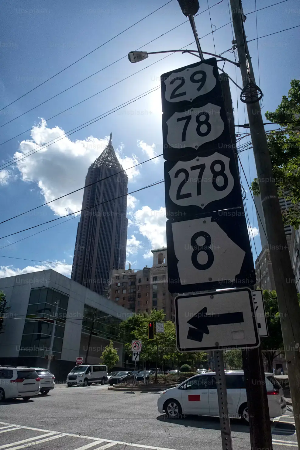 Downtown street intersection with multiple highway route signs and a tall skyscraper in the background.