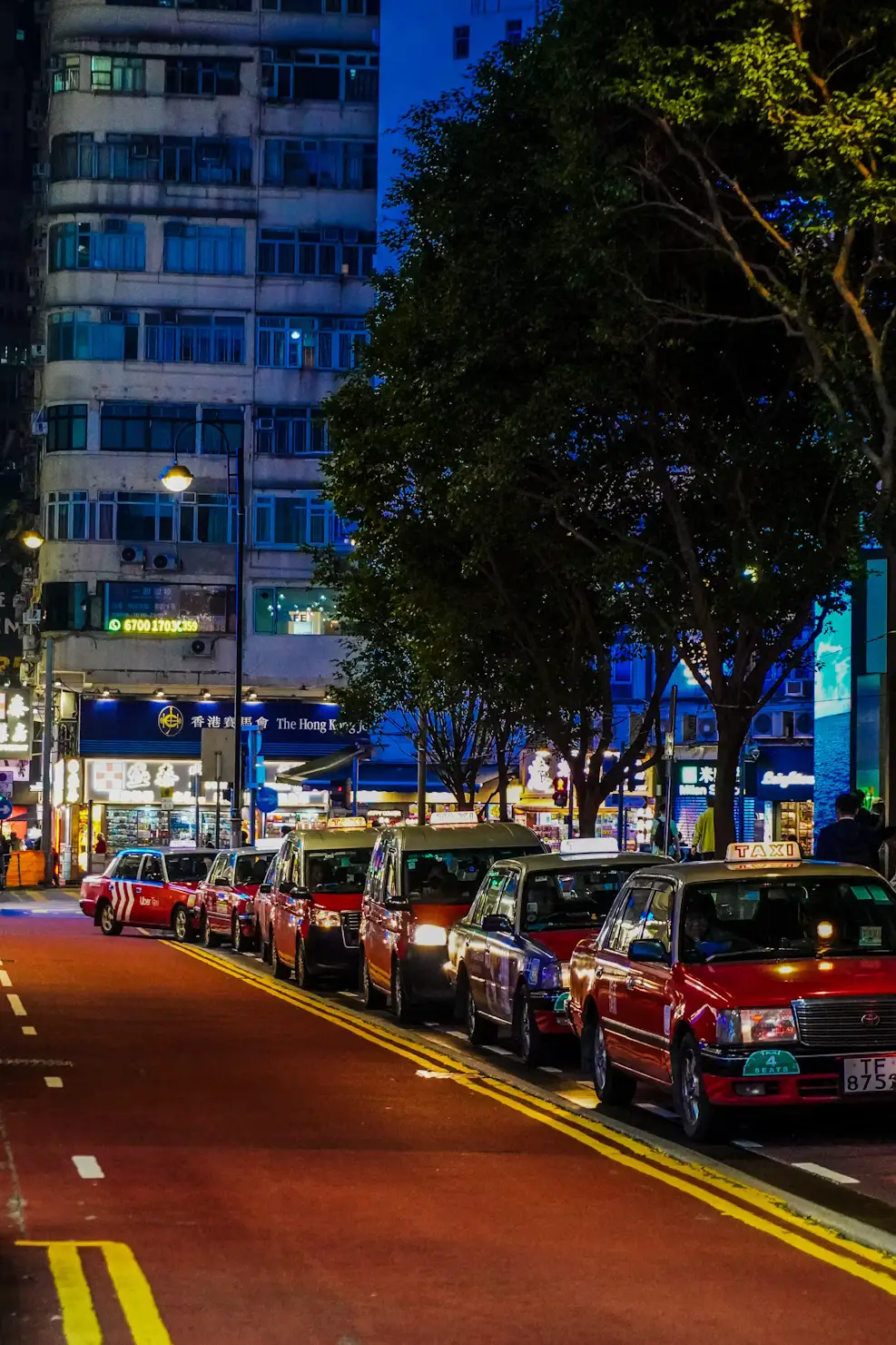Busy city street lined with red taxis and high-rise buildings at dusk in Hong Kong.