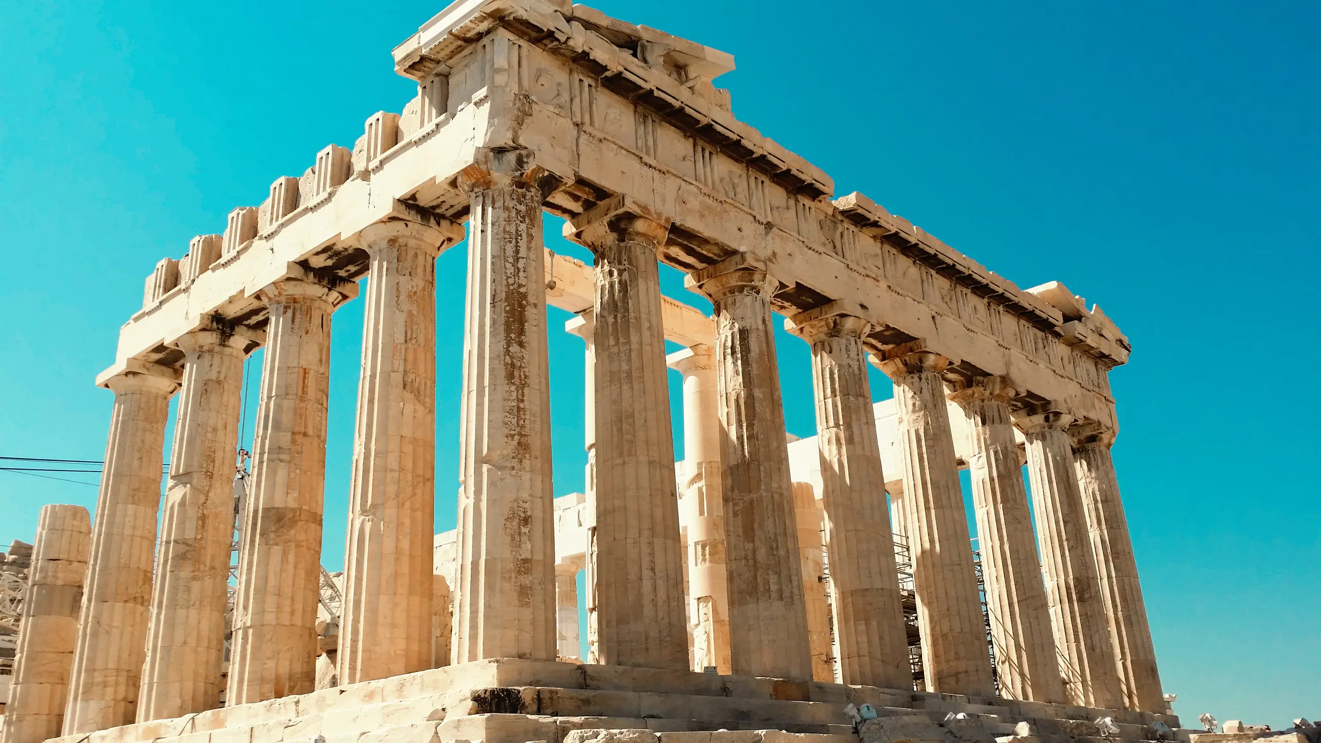 The Parthenon on the Acropolis of Athens, a Doric-columned marble temple viewed from its front facade under a bright blue sky.