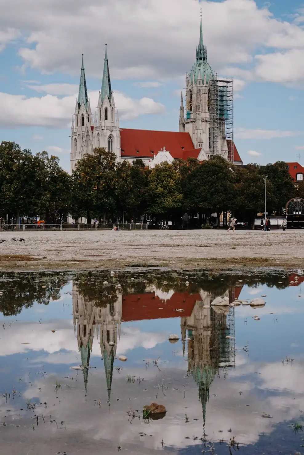 Twin-spired church reflected in a puddle with surrounding trees