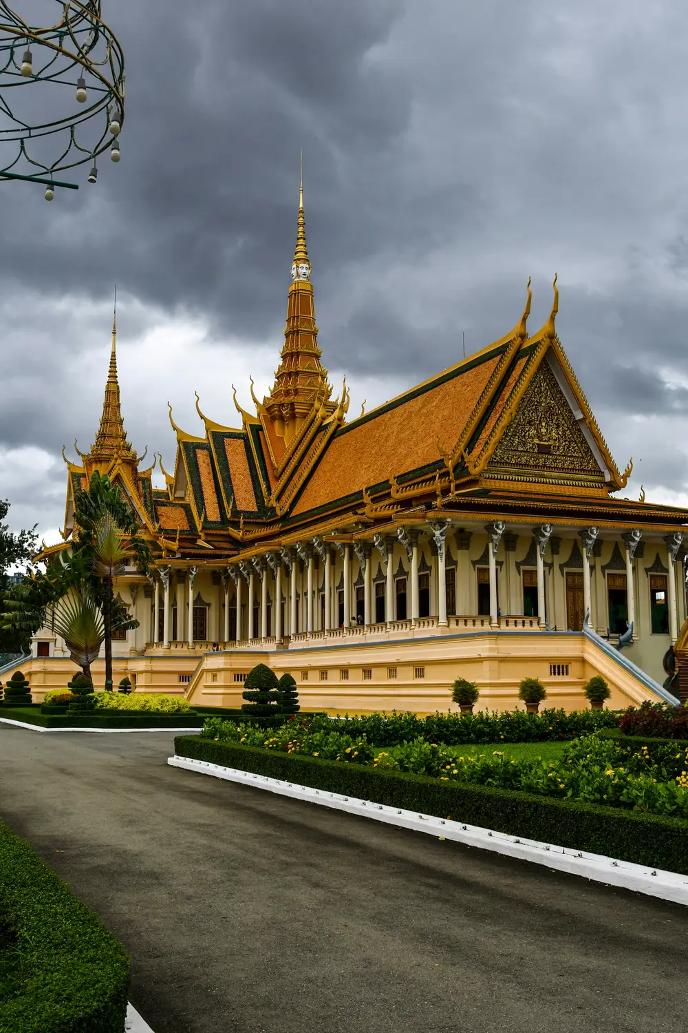 Grand golden throne hall of the Royal Palace with manicured gardens under dramatic stormy sky, Phnom Penh, Cambodia