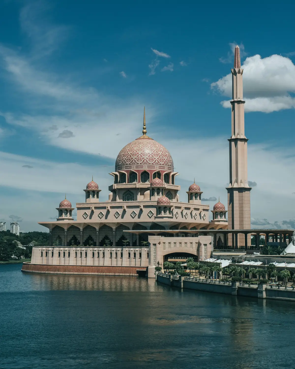 Putra Mosque pink dome and minaret reflecting on Putrajaya Lake with blue sky and clouds in Malaysia