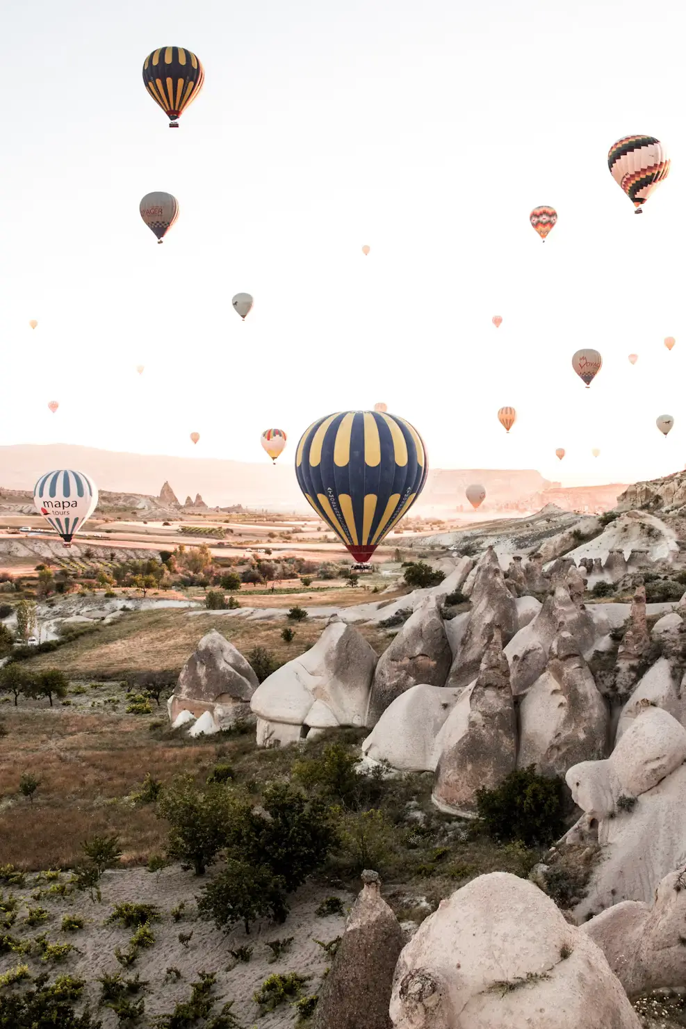 Numerous hot air balloons rising above the rocky, cone-shaped rock formations of Cappadocia, Turkey.