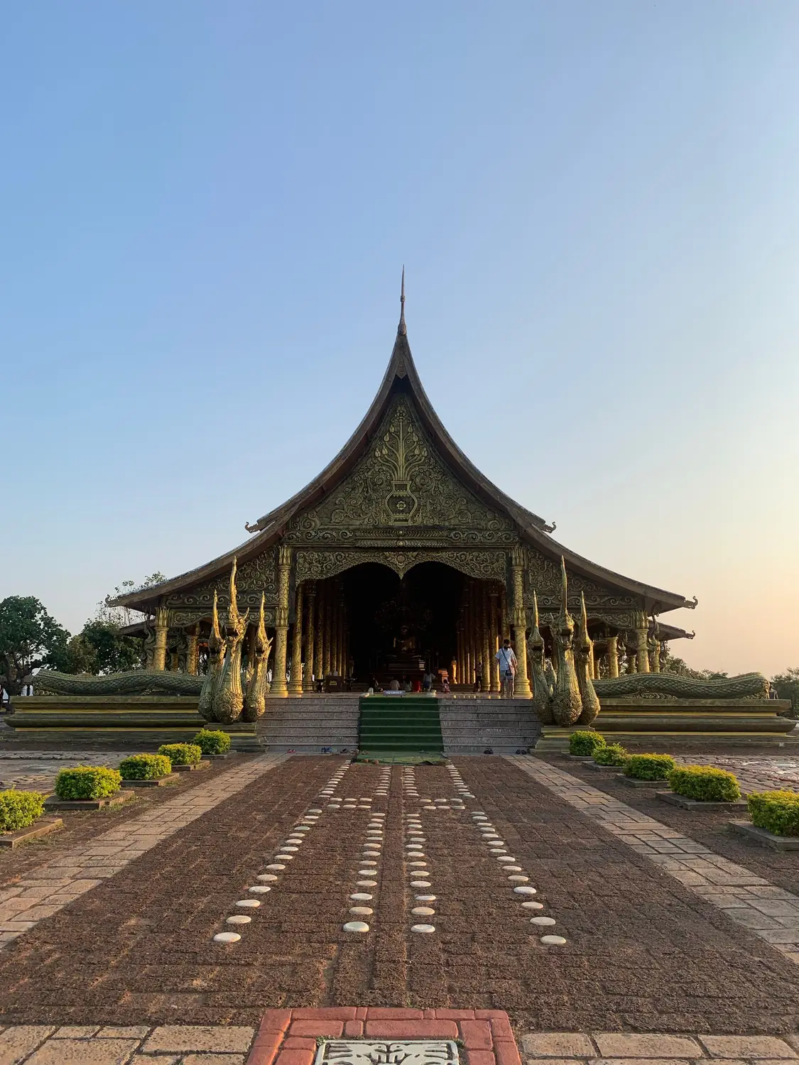 Traditional Lao pavilion with a pointed roof at the end of a brick pathway at dusk in Laos.
