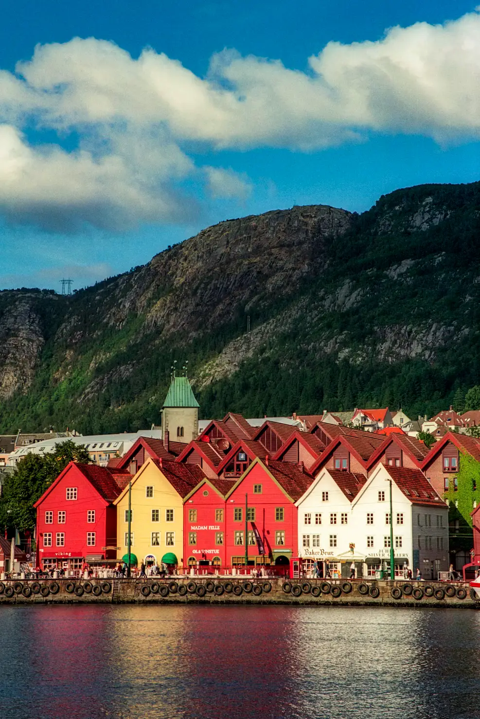 The colourful wooden buildings of Bergen's Bryggen wharf reflected in the harbour, with a mountain rising behind.