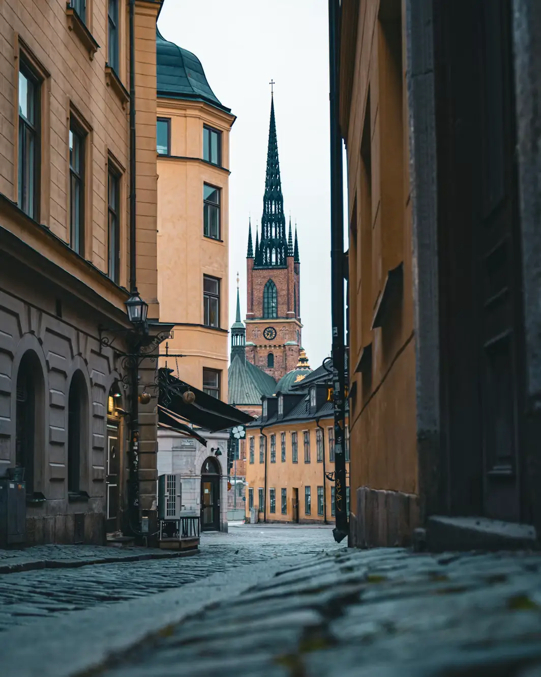 Narrow cobblestone alley between old buildings, with a church spire visible ahead.