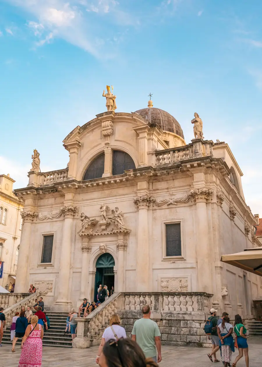 Baroque church facade with a domed bell tower, people walking on the steps below.