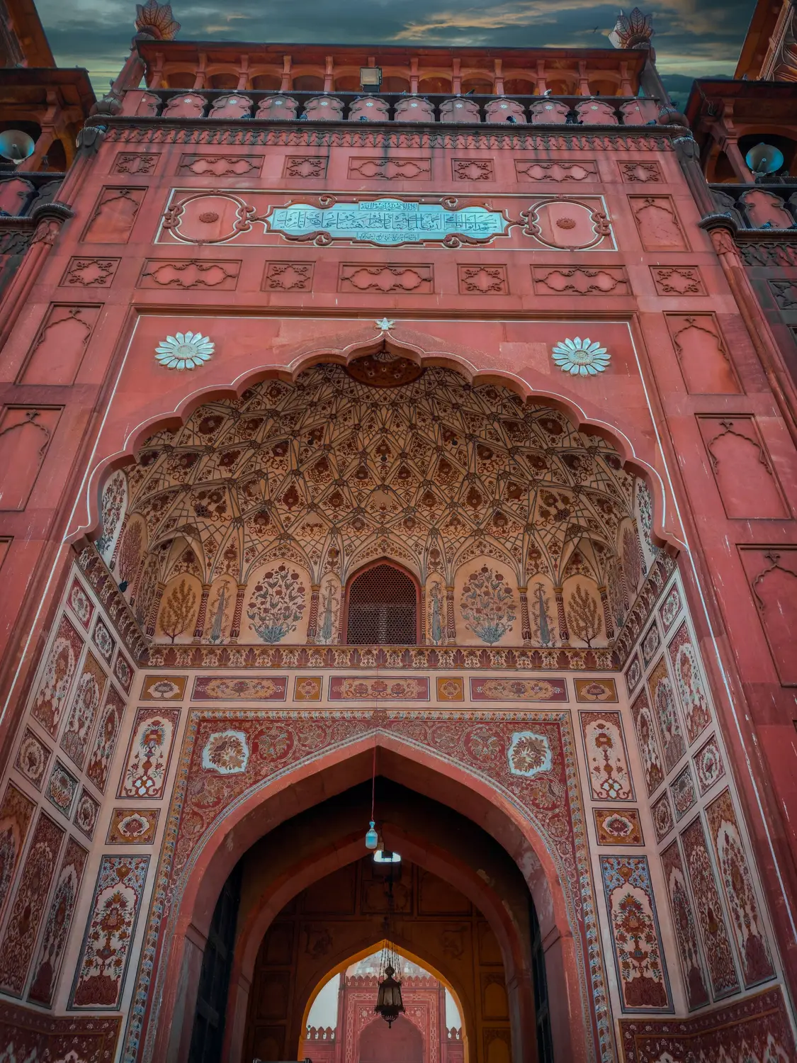 Intricate Mughal arch gateway with detailed floral stonework looking up Lahore Pakistan