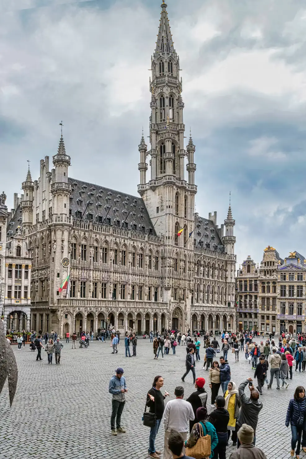 The ornate Gothic tower of Brussels' Town Hall rising above the Grand Place, with tourists gathered in the cobblestone square.