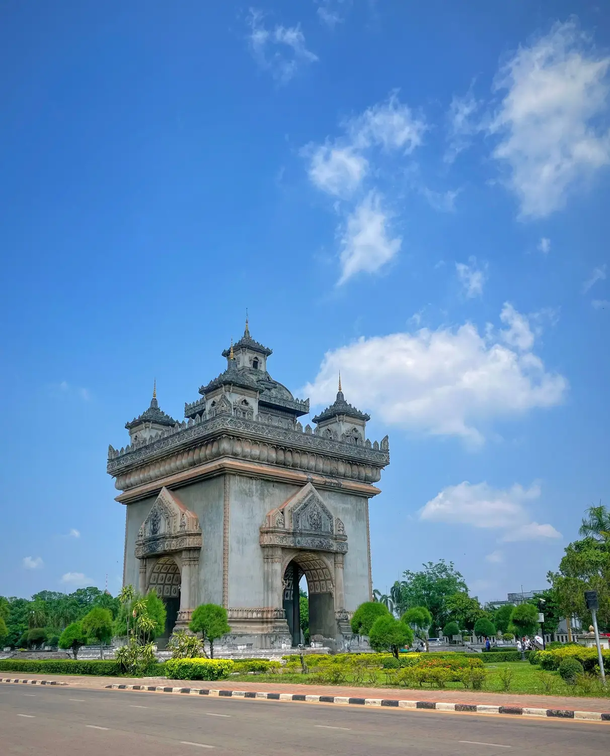 Patuxai victory monument arch surrounded by greenery under a bright blue sky in Vientiane, Laos.