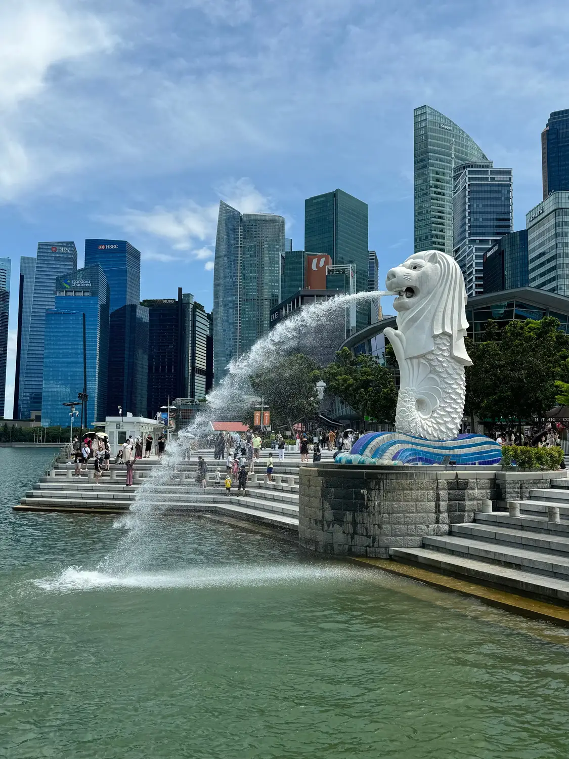 Merlion statue spouting water at Marina Bay with Singapore skyline skyscrapers and tourists in foreground