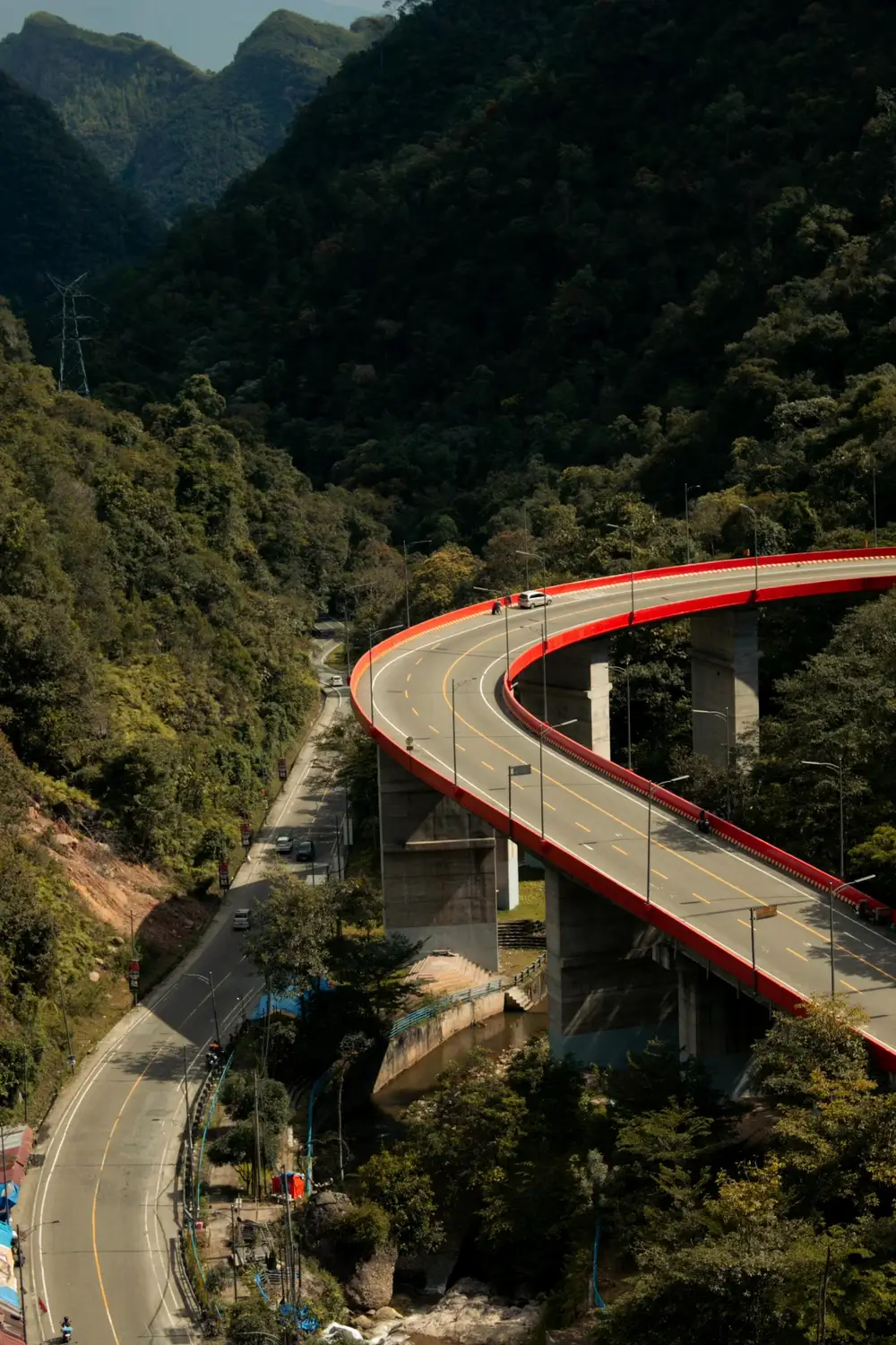 Curving red-railed elevated highway viaduct winding through lush green forested mountains