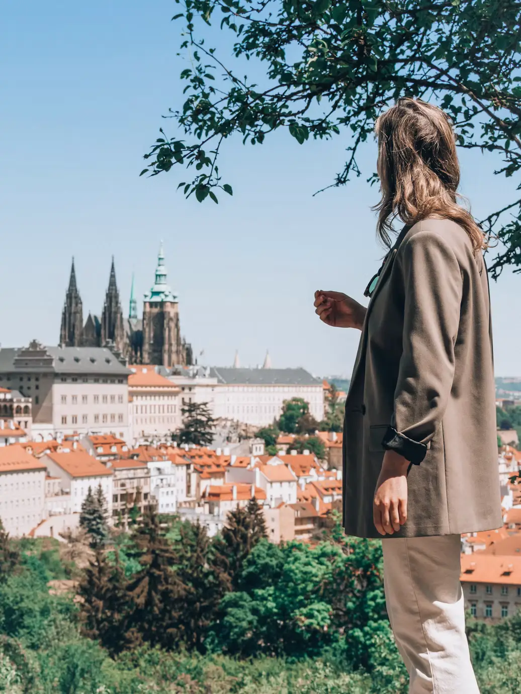 Person looking out over Prague's rooftops and Prague Castle from a hillside viewpoint