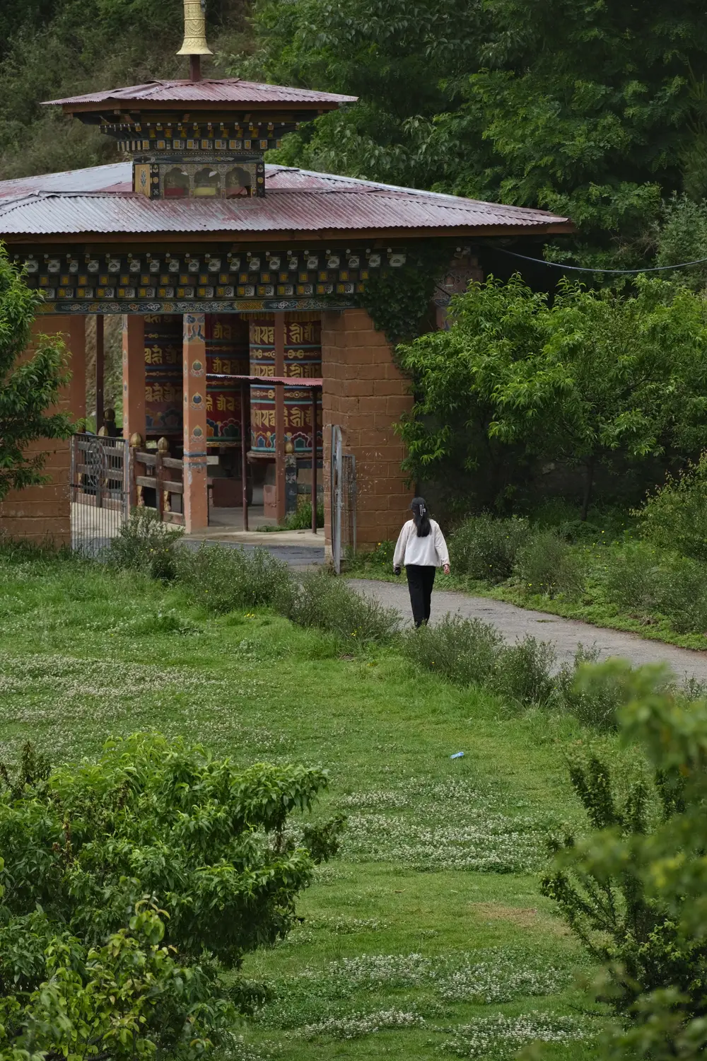 Traditional Bhutanese watchtower with a person walking along a grassy path through the countryside in Bhutan.