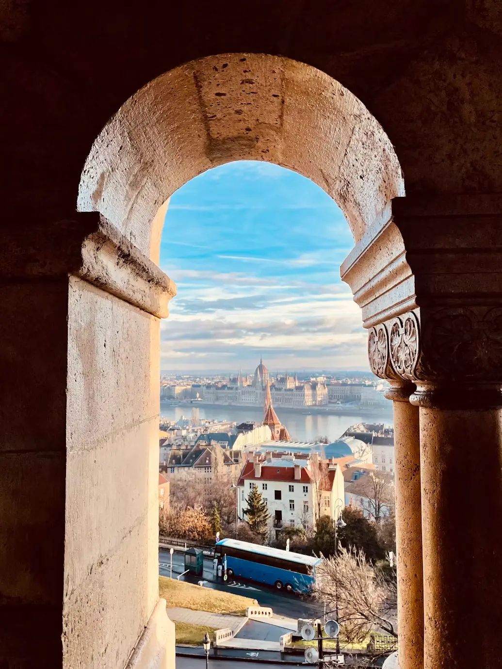 Stone archway framing a riverside city skyline with a grand parliament building across the river.