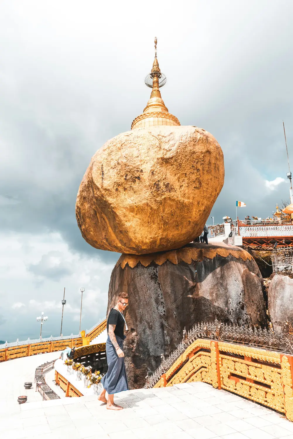 Tourist standing barefoot beside the famous Kyaiktiyo Golden Rock balancing boulder with small pagoda on top, Mon State Myanmar