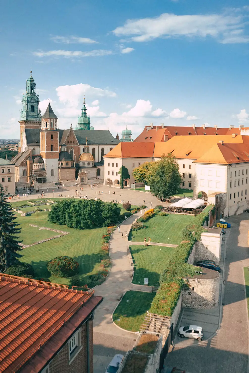 Historic Polish church and landscaped courtyard viewed from above, surrounded by traditional red-roofed buildings.