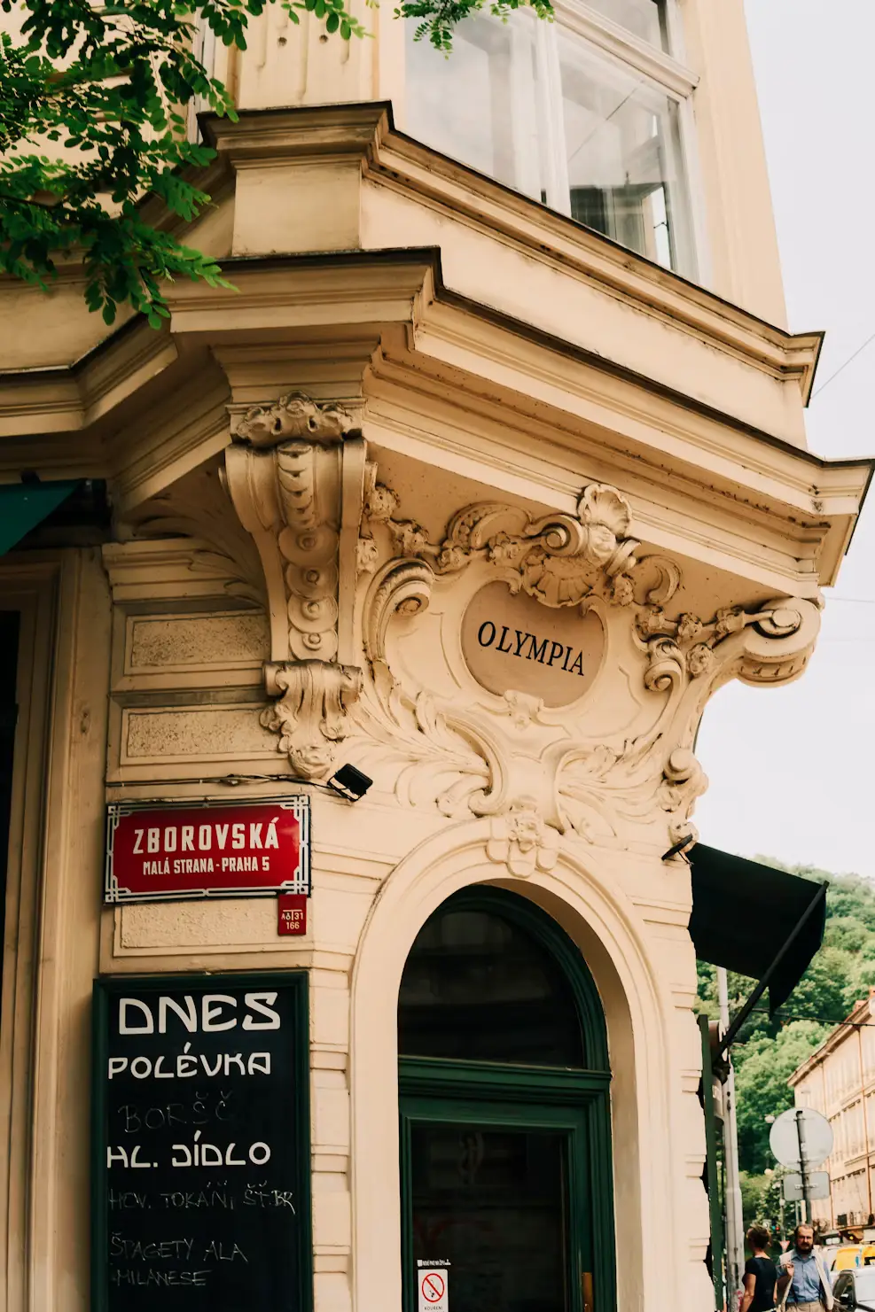 Ornate corner facade of a Prague building with a chalkboard menu sign advertising the day's soup outside a café